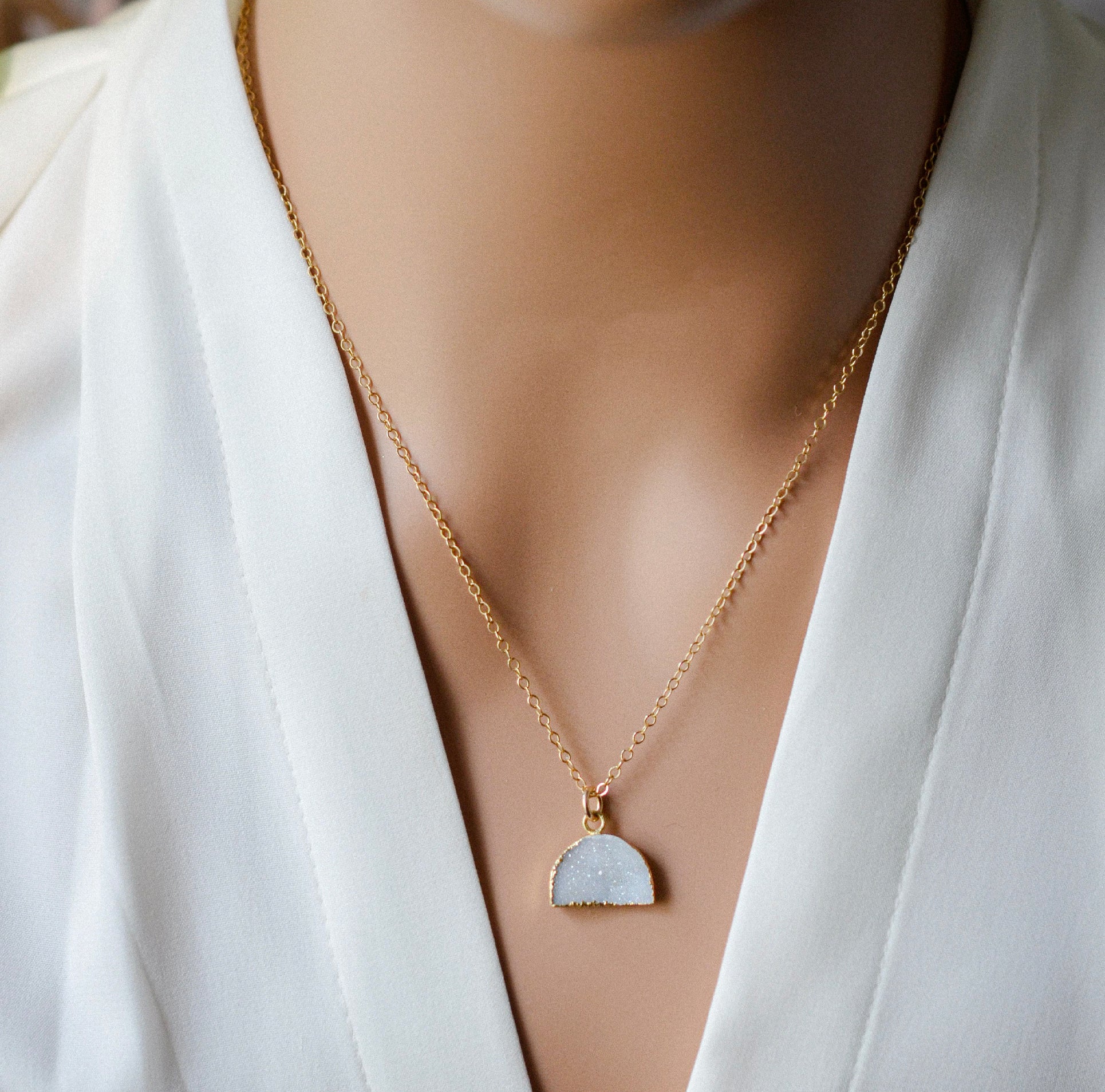 Modeled image. This necklace is handmade with a natural white druzy quartz pendant in a half-circle or crescent shape. Available in 14k gold filled.