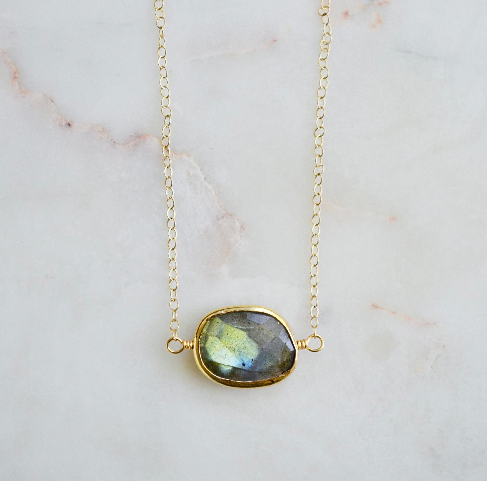 A faceted, natural labradorite pendant bezeled in gold and set on a 14k gold filled chain. This necklace is also available in sterling silver. The stone is oval in shape and flashes blue, green, or yellow.