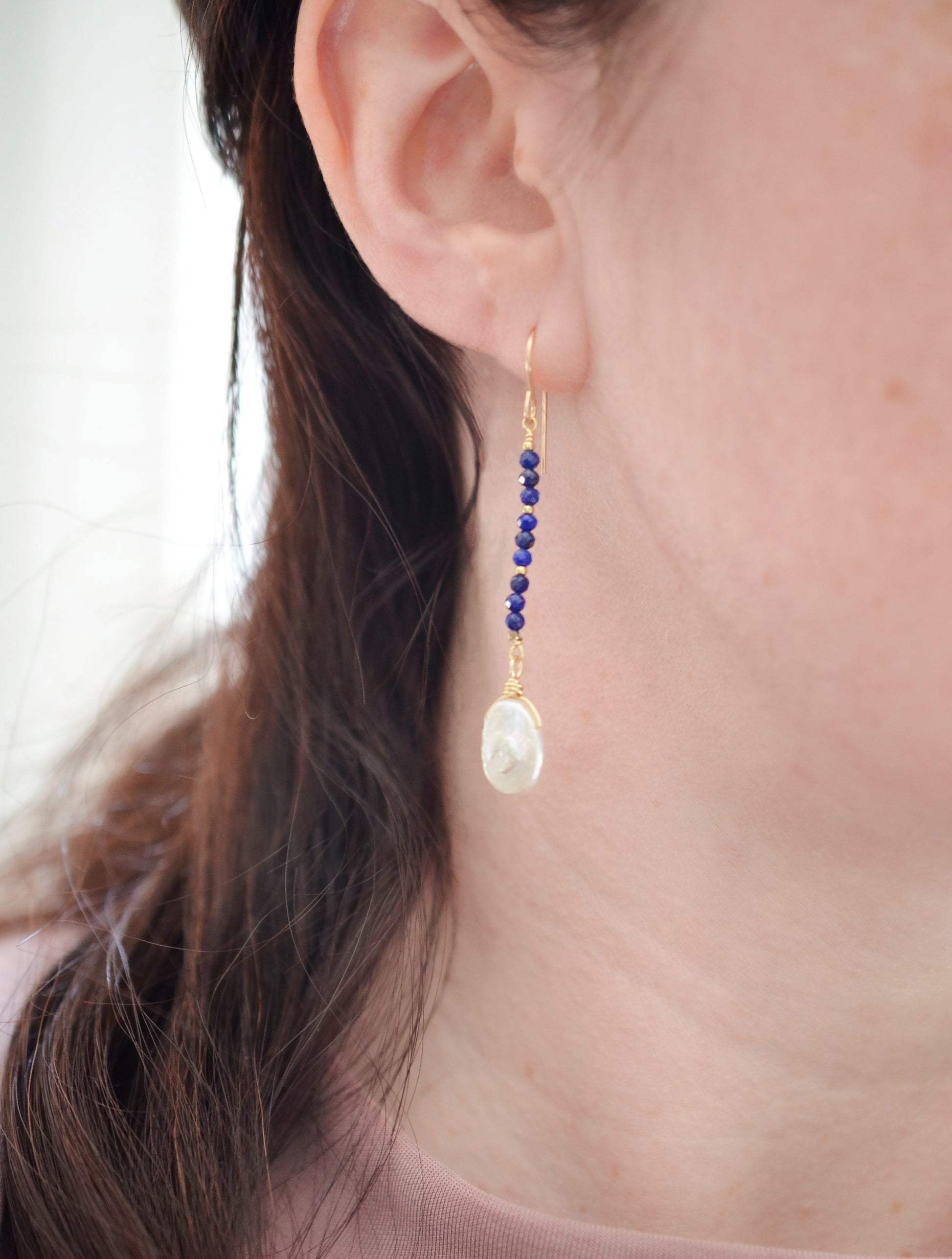 Natural blue lapis lazuli gemstone and white freshwater pearl long dangle earrings. The dangles are long and thin with oval freshwater pearls at the end. They come in 14k gold filled and sterling silver and a great gift for mom, girlfriend, anniversary, or yourself. Modeled image.