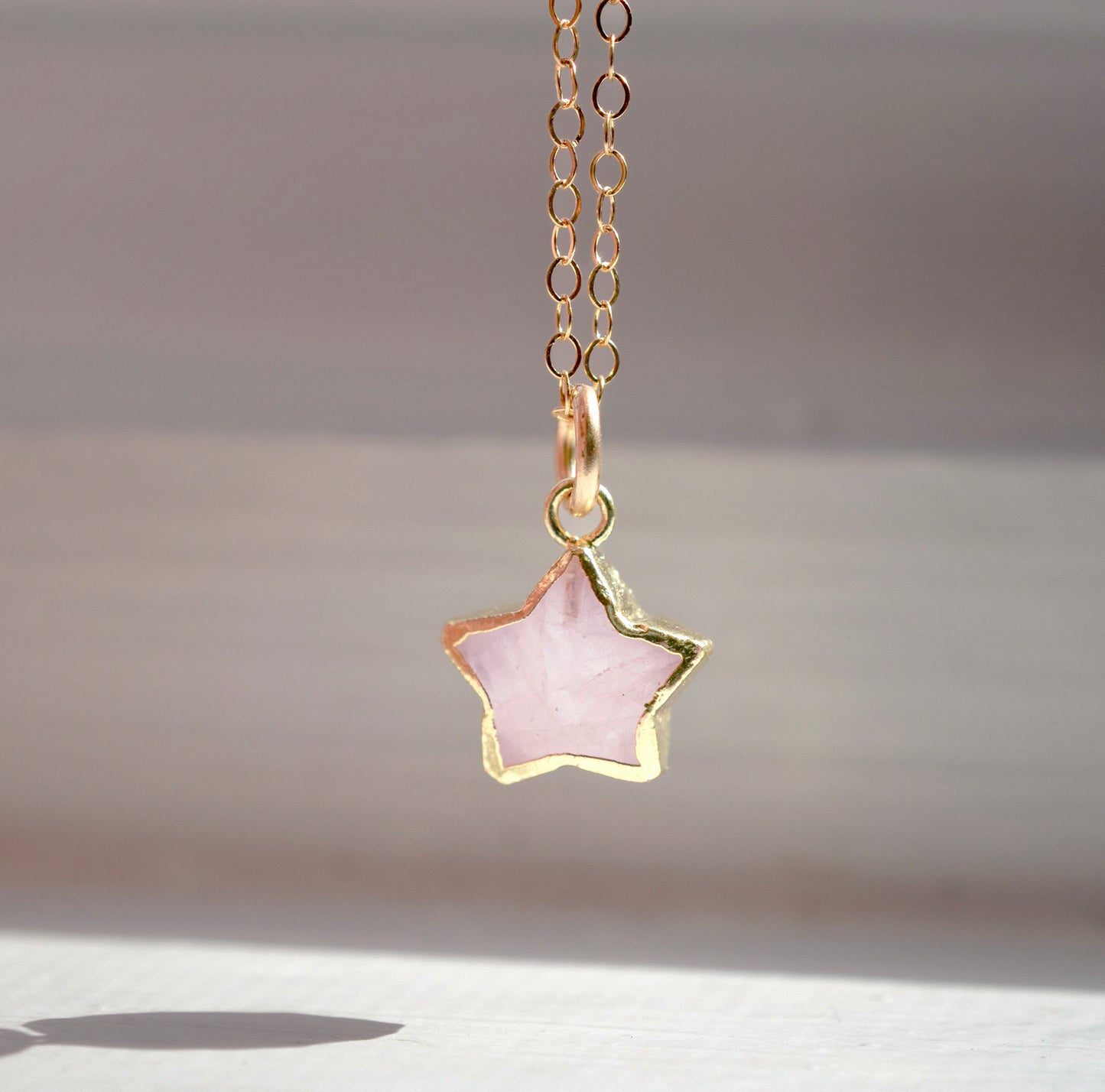 Dainty rose quartz star pendant necklace on a gold chain.