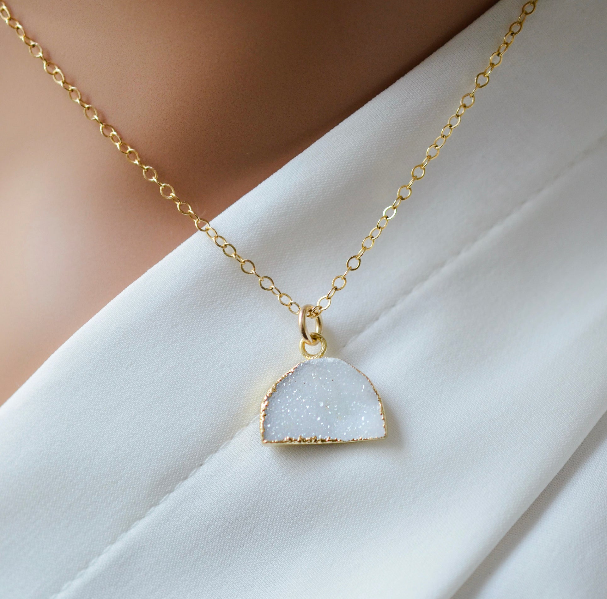 A gold-filled half moon shaped necklace with a milky white quartz druzy centerpiece.