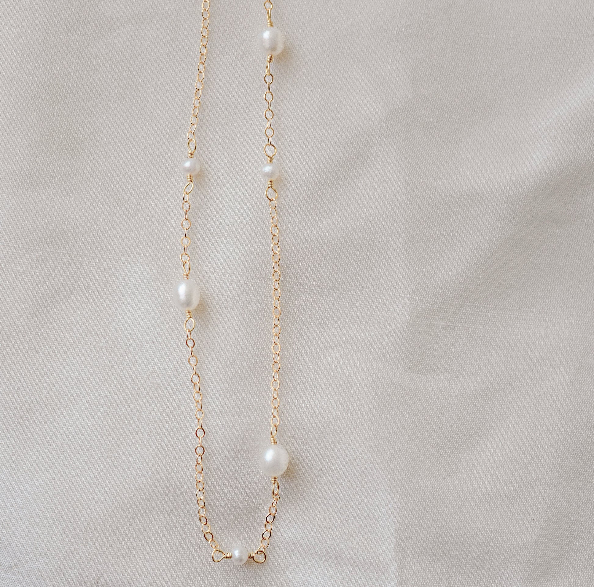 Genuine white freshwater pearls of varying sizes alter on this chain necklace. The gold style is shown.