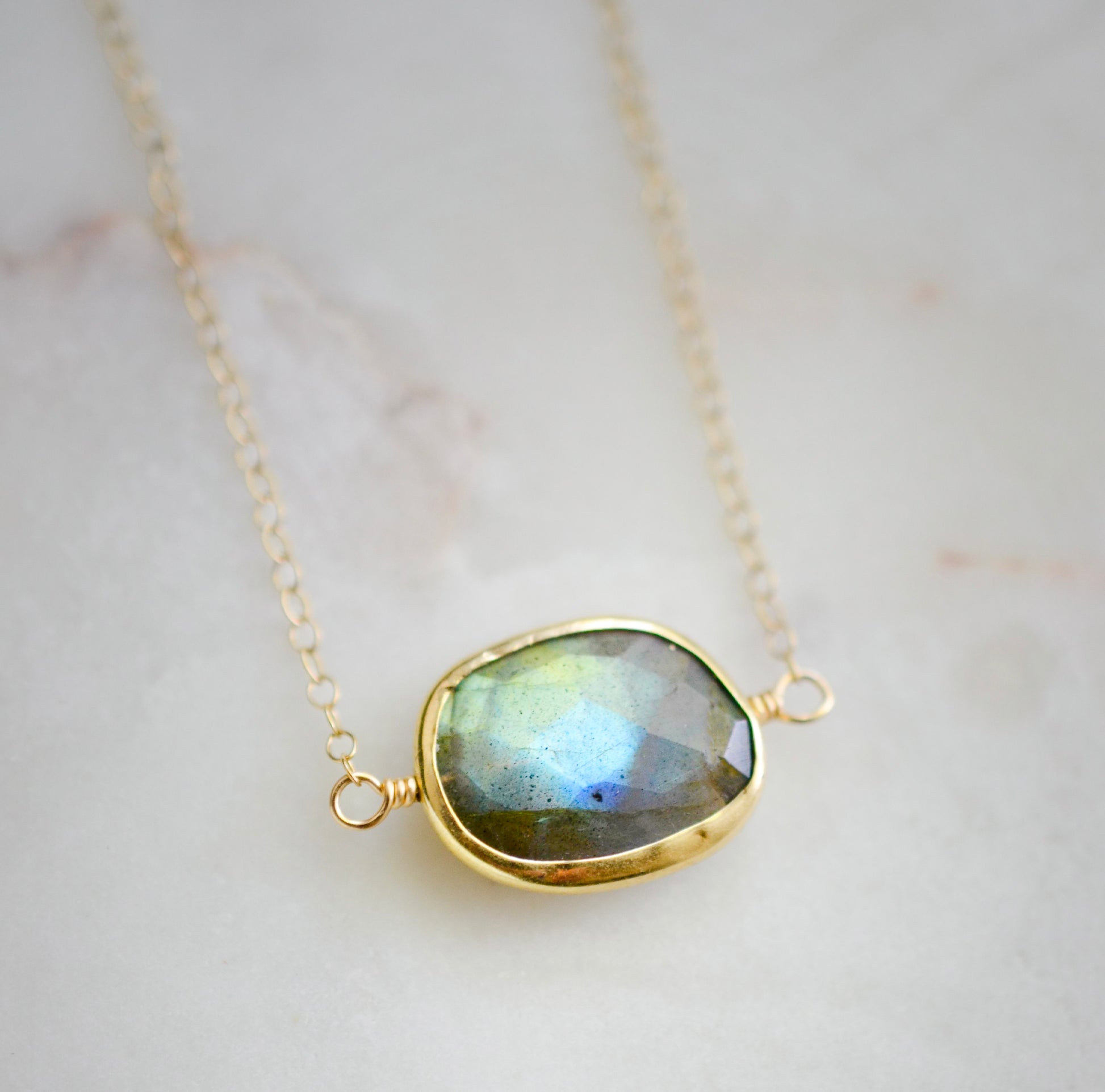 Necklace with a gold-framed Labradorite stone on a light background. The handmade pendant is bezeled in gold and set on a 14k gold filled chain. This necklace is also available in sterling silver. The stone is oval in shape and flashes blue, green, or yellow.