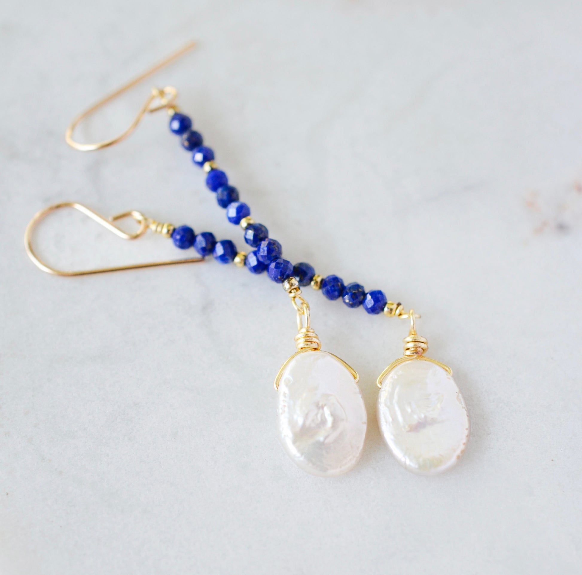 Natural blue lapis lazuli gemstone and white freshwater pearl long dangle earrings. The dangles are long and thin with oval freshwater pearls at the end. They come in 14k gold filled and sterling silver.