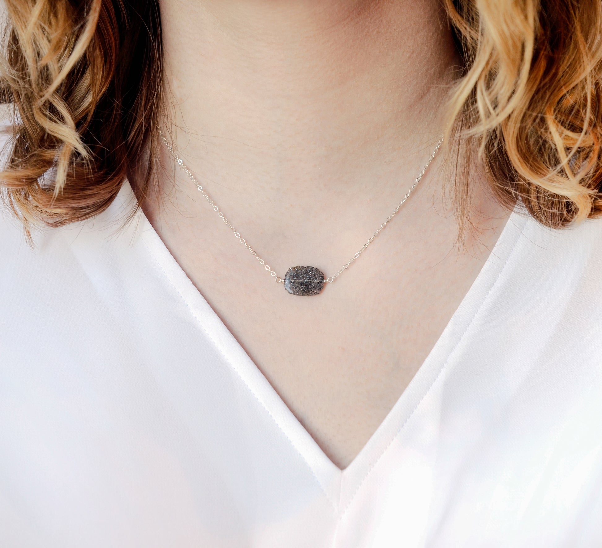Genuine raw black sunstone gemstone set on a sterling silver chain. The shape of the stone is irregular. Modeled image.