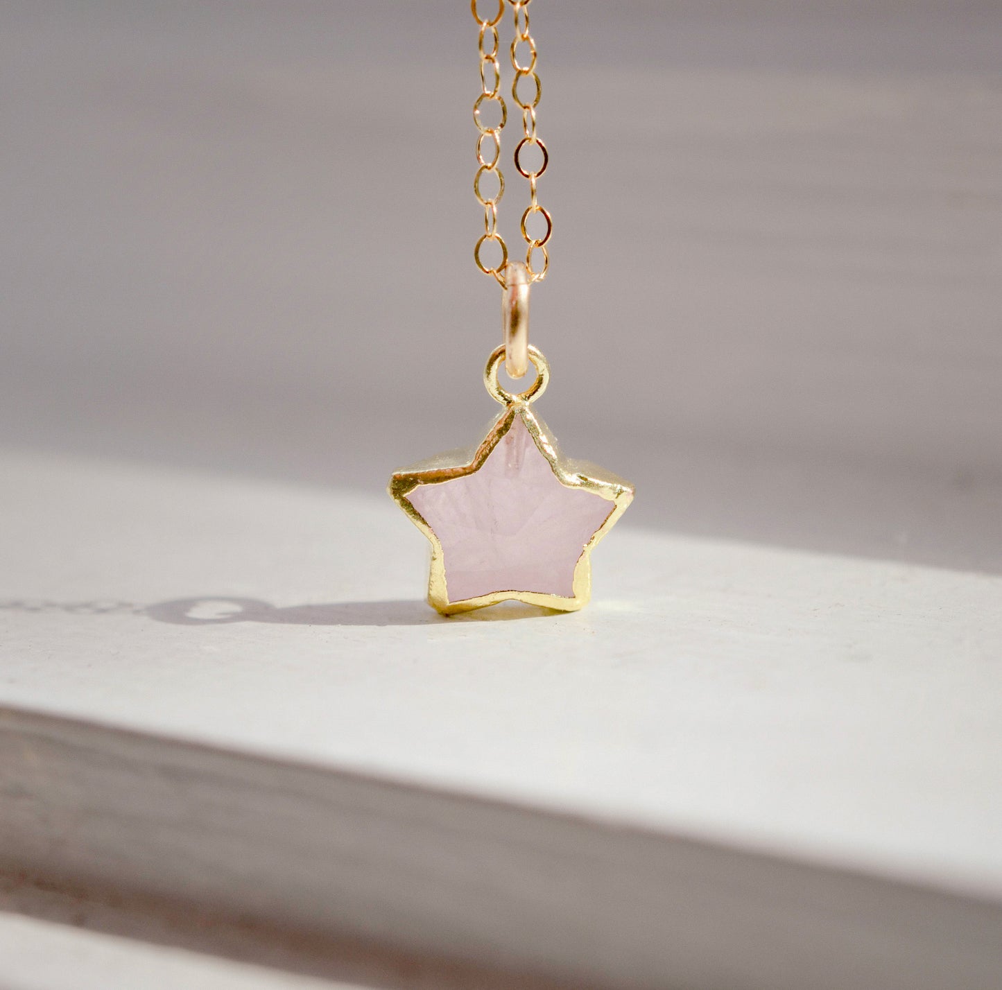 Dainty rose quartz star pendant necklace on a gold chain.