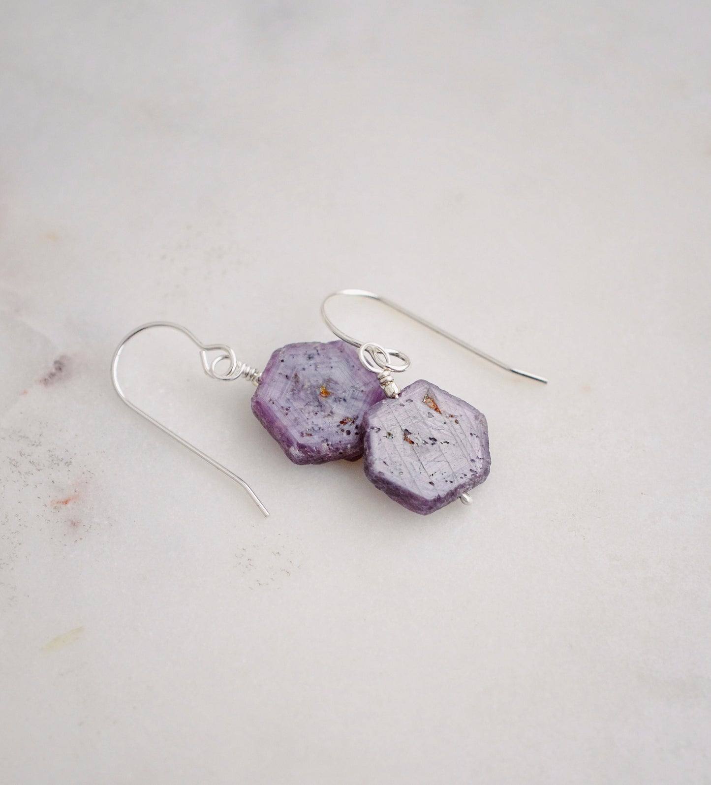 Purple-pink raw ruby stones suspended from sterling silver earwires. The stones are rough and in their natural hexagonal shape. 