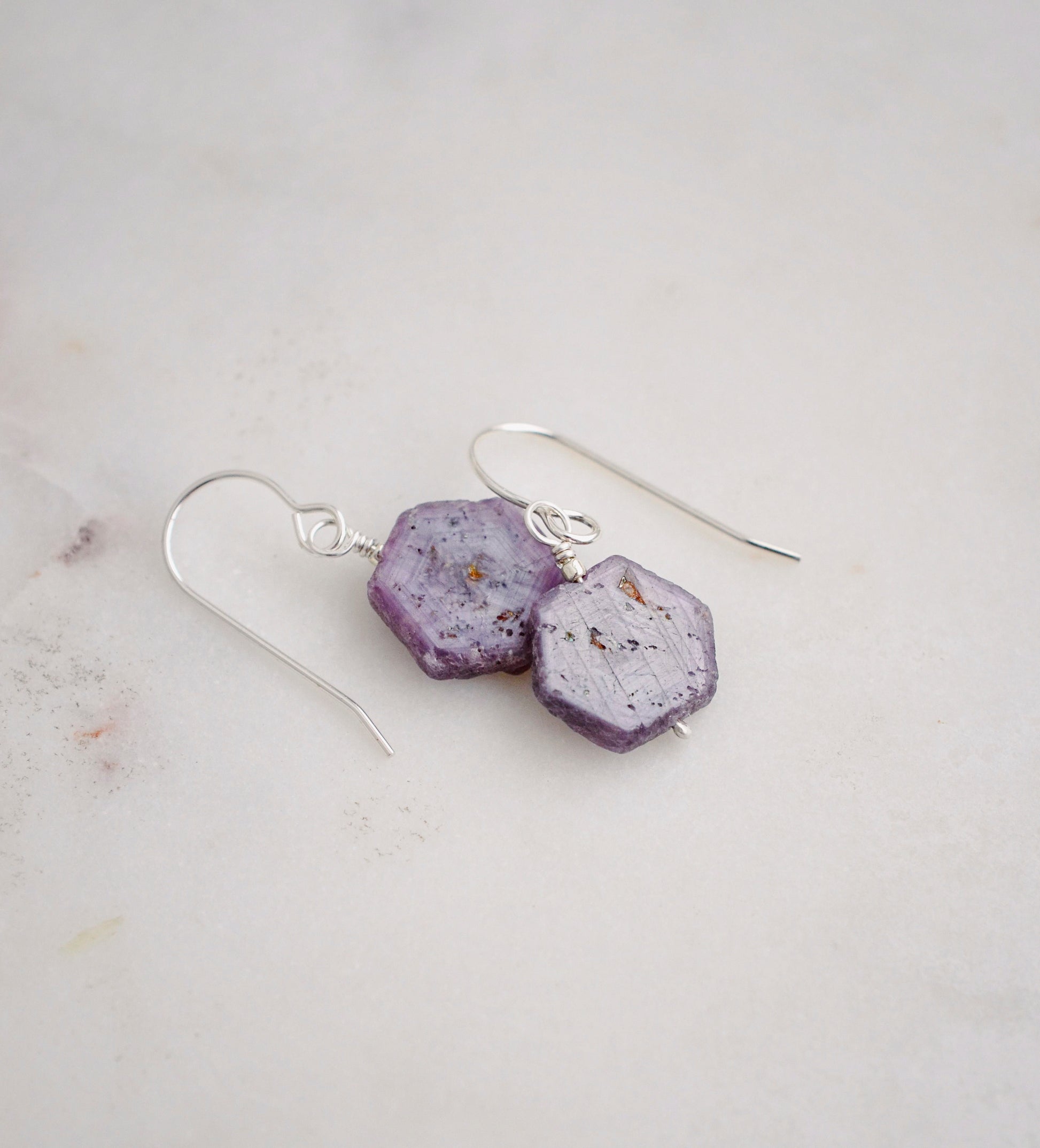 Purple-pink raw ruby stones suspended from sterling silver earwires. The stones are rough and in their natural hexagonal shape.