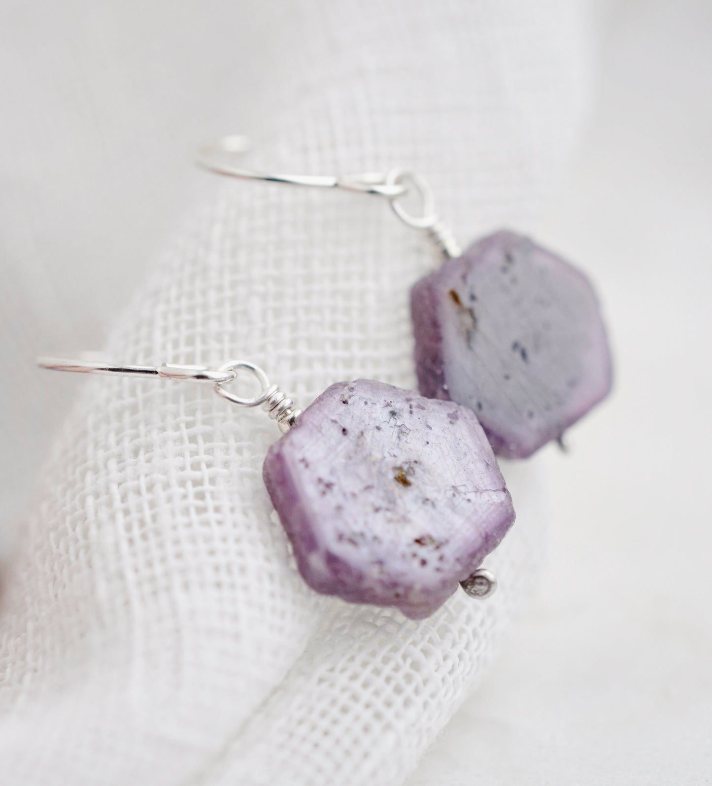 Purple-pink raw ruby stones suspended from sterling silver earwires. The stones are rough and in their natural hexagonal shape. 