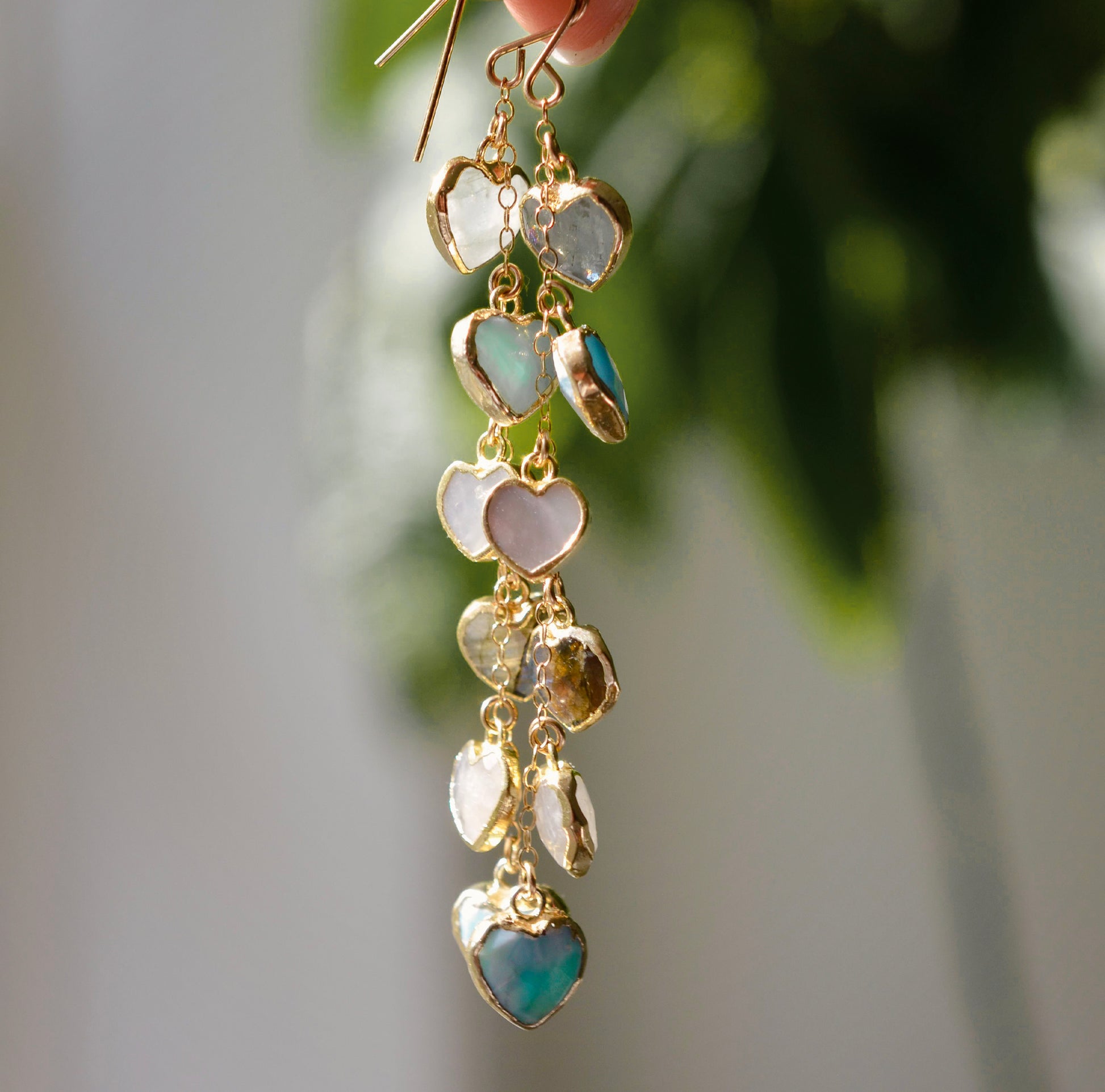 These handmade earrings feature blue and white natural stone hearts bezeled in gold. Each gemstone is a different color and includes: labradorite, larimar, mother of pearl, aquamarine, and rainbow moonstone. Long and light weight they make the perfect romantic gift. They are 3 inches long.
