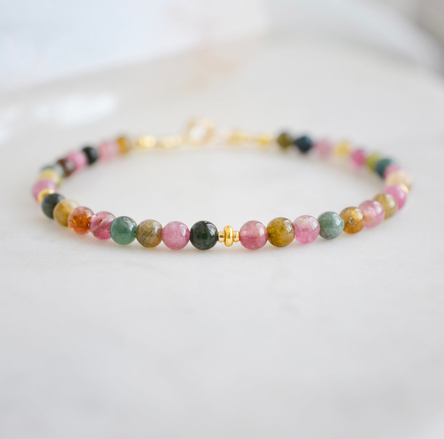 Multi color genuine tourmaline crystals on a handmade beaded bracelet. Shown in gold. Close up of stones.