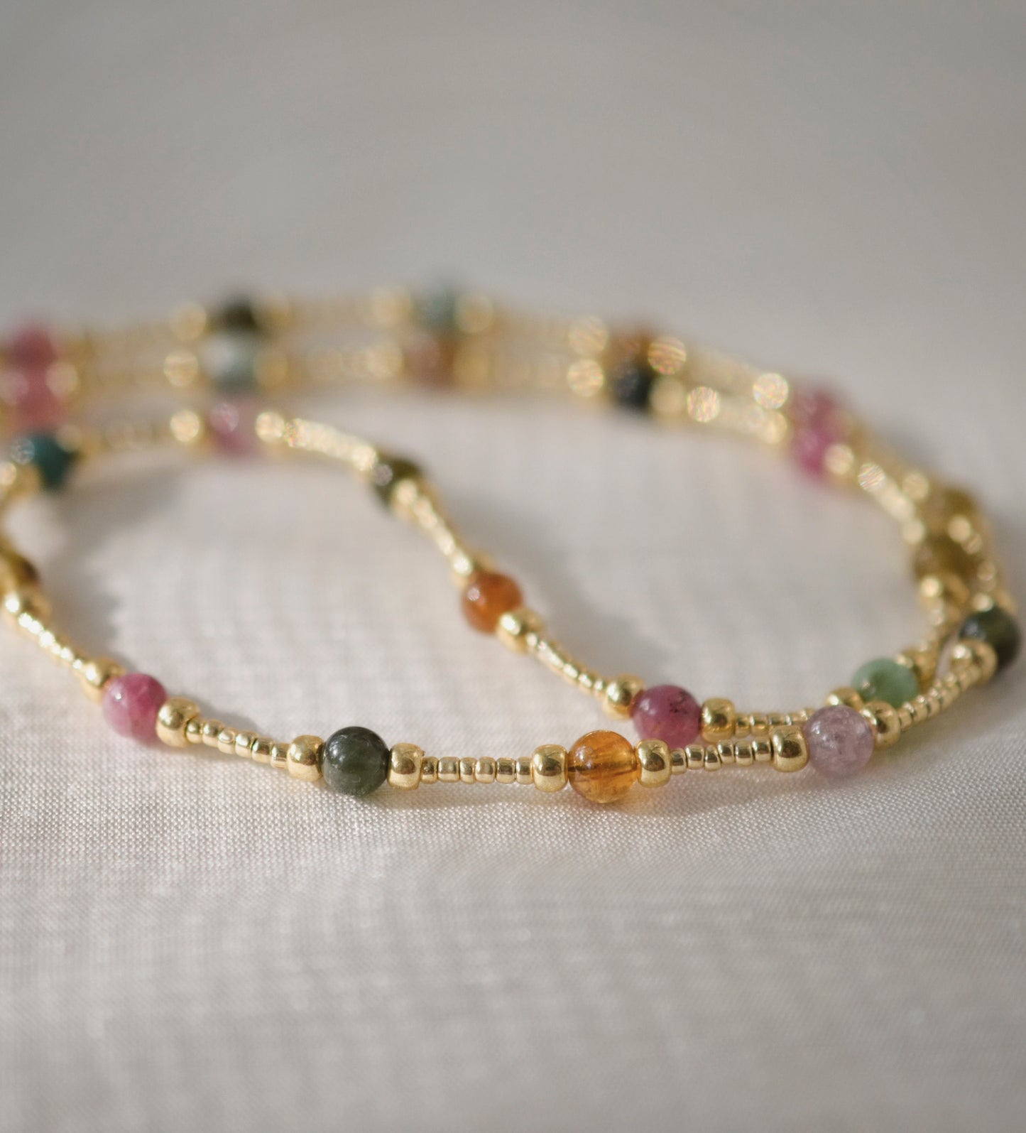 Multicolored, smooth polished Tourmaline gems hand-beaded with gold plated glass beads. Colors range from pink, green, brown, yellow, or black.