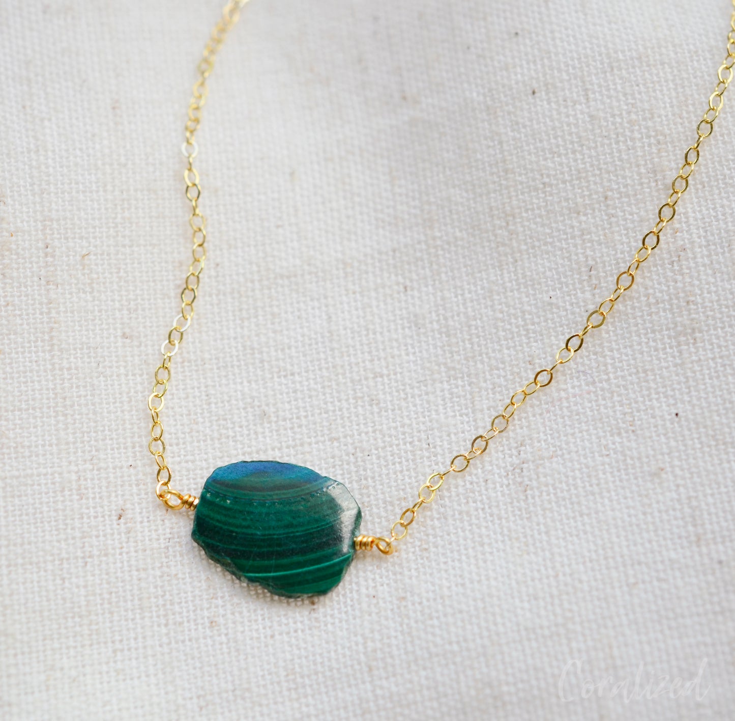 Natural green Malachite smooth polished slice with raw edges. Each stone is an irregular oval shape and has a variety of banding. Shown on a 14k gold filled chain.
