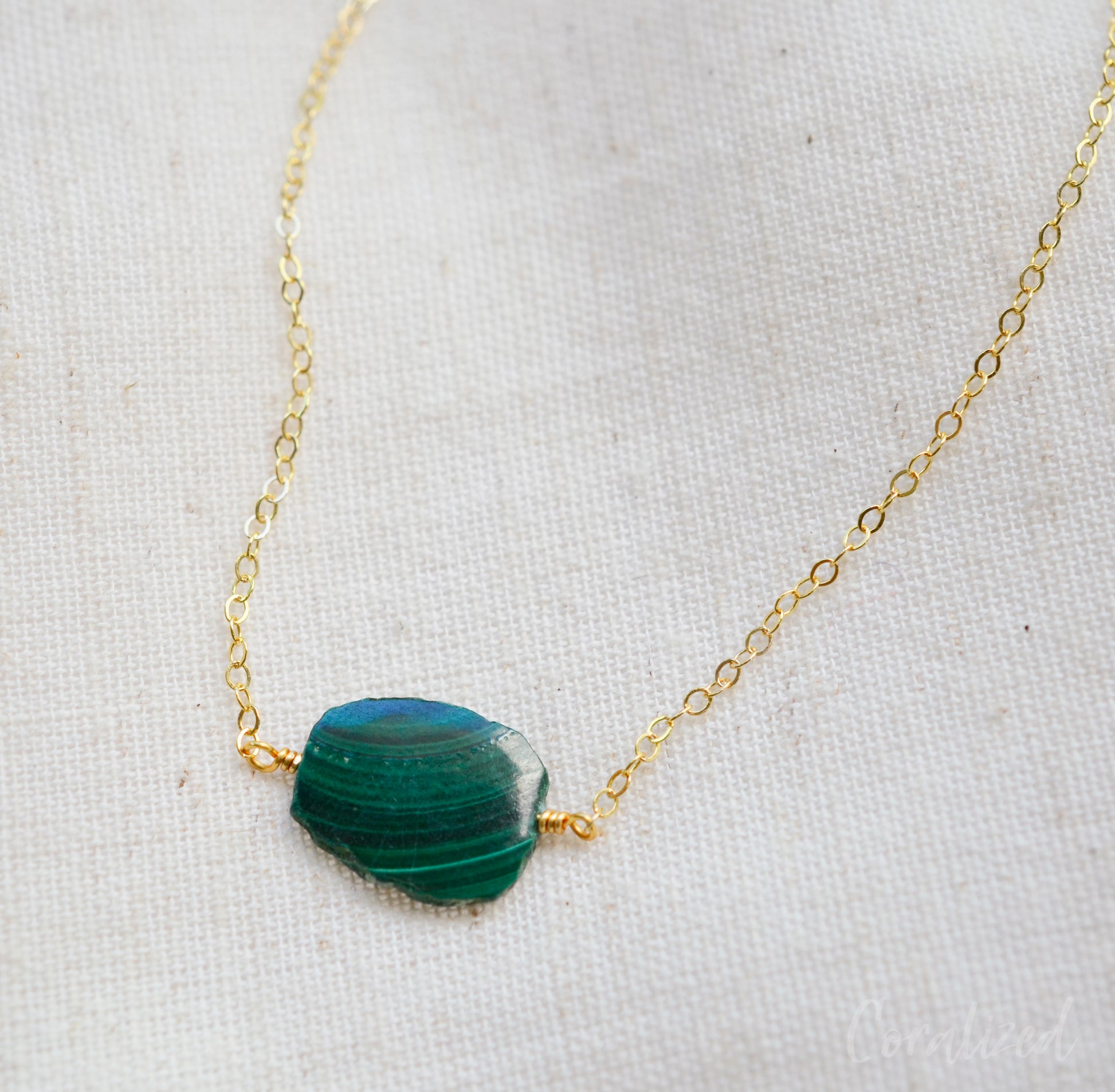 Natural green Malachite smooth polished slice with raw edges. Each stone is an irregular oval shape and has a variety of banding. Shown on a 14k gold filled chain.