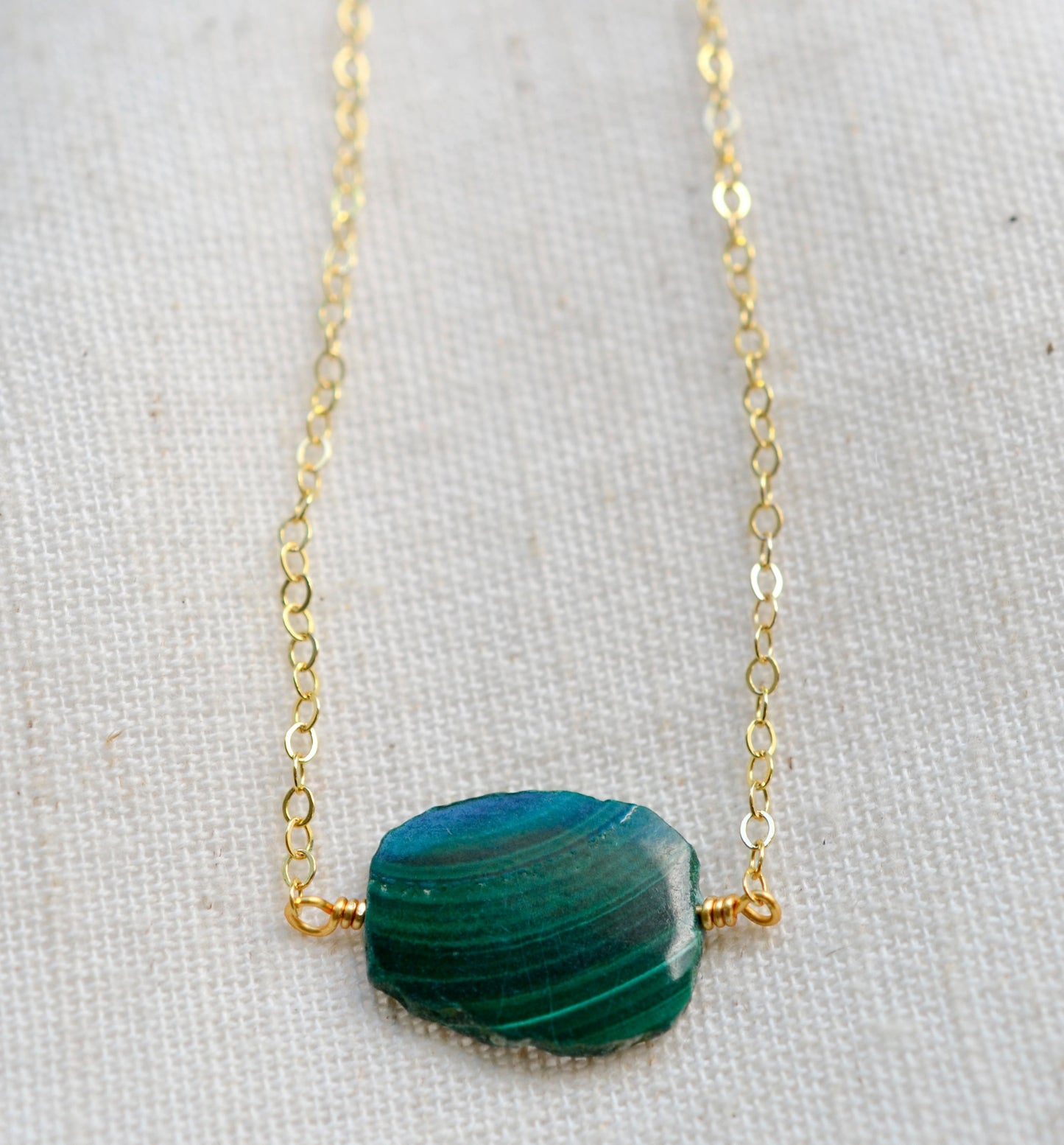 Natural green Malachite smooth polished slice with raw edges. Each stone is an irregular oval shape and has a variety of banding. Shown on a 14k gold filled chain.