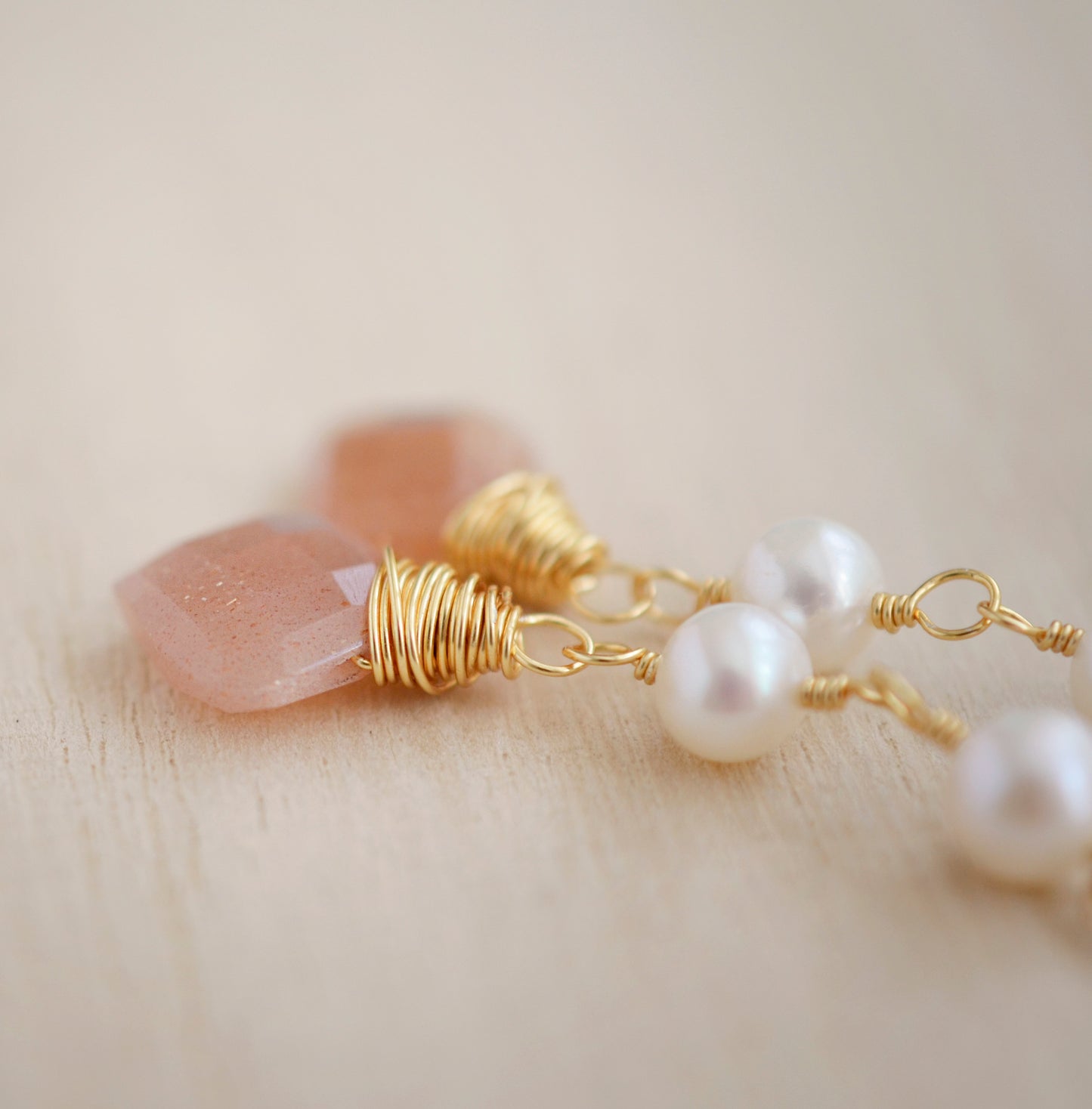 Two white semi-round pearls hang over natural peach Moonstone faceted drops. The gold style is shown.