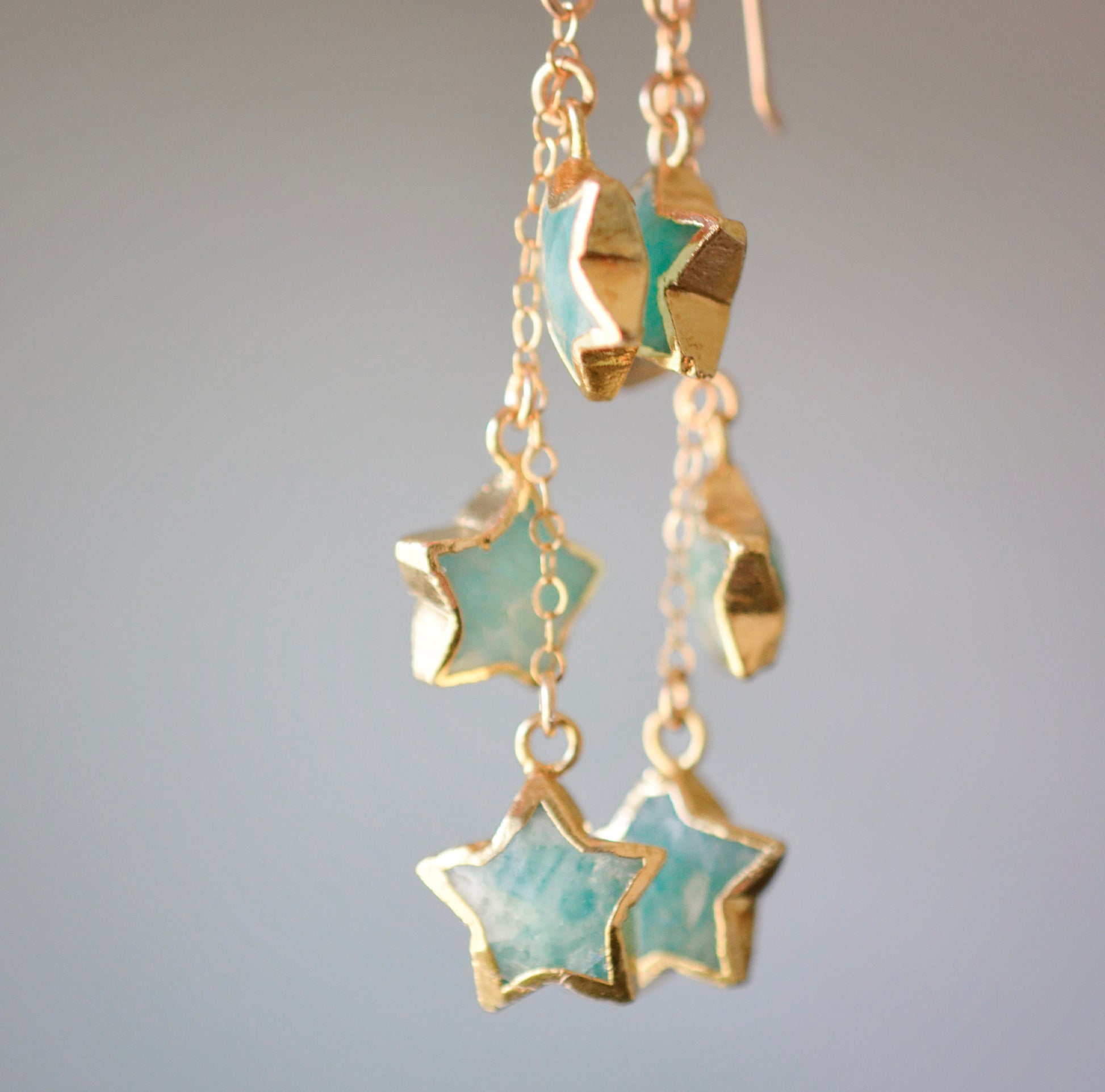 Close up of blue-green natural amazonite star shaped stones set on long dangles in gold.