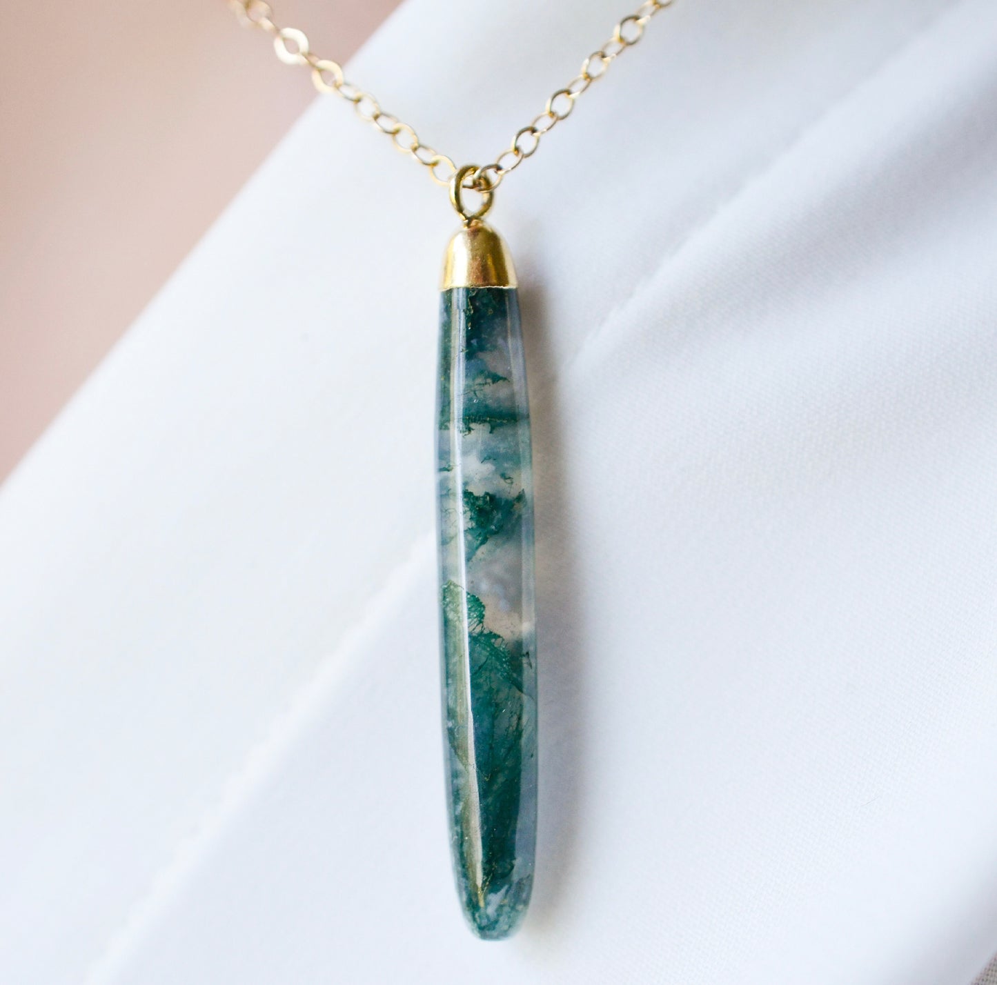 Long green, white, and clear real natural moss agate stone set on a 14k gold filled chain. The pendant is a long thin oval shape.