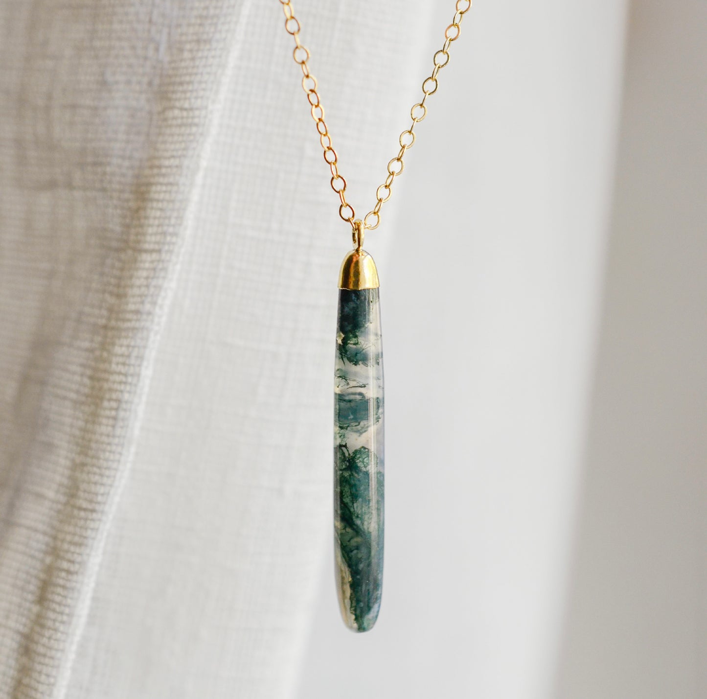 Long green, white, and clear real natural moss agate stone set on a 14k gold filled chain. The pendant is a long thin oval shape.