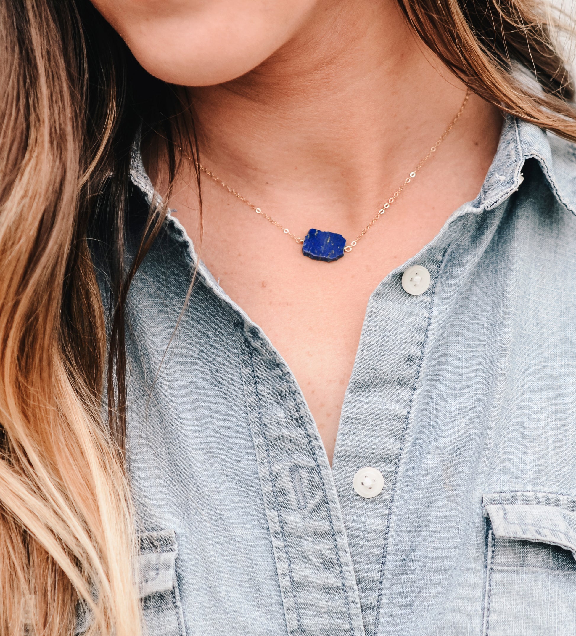 Natural blue lapis lazuli slice set onto a sterling silver chain. The stone is smooth polished with raw edges and oval in shape. Natural pyrite and calcite flecks are visible within each stone. Modeled image.