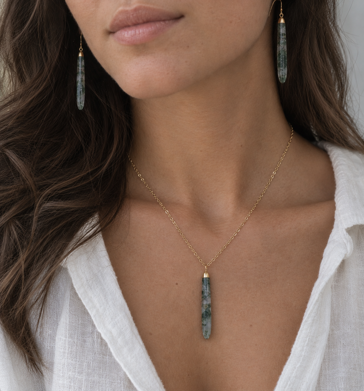 A woman wearing a matching moss agate pendant necklace and earrings set. The jewelry is handmade in 14k gold filled with 18k gold electroplate.