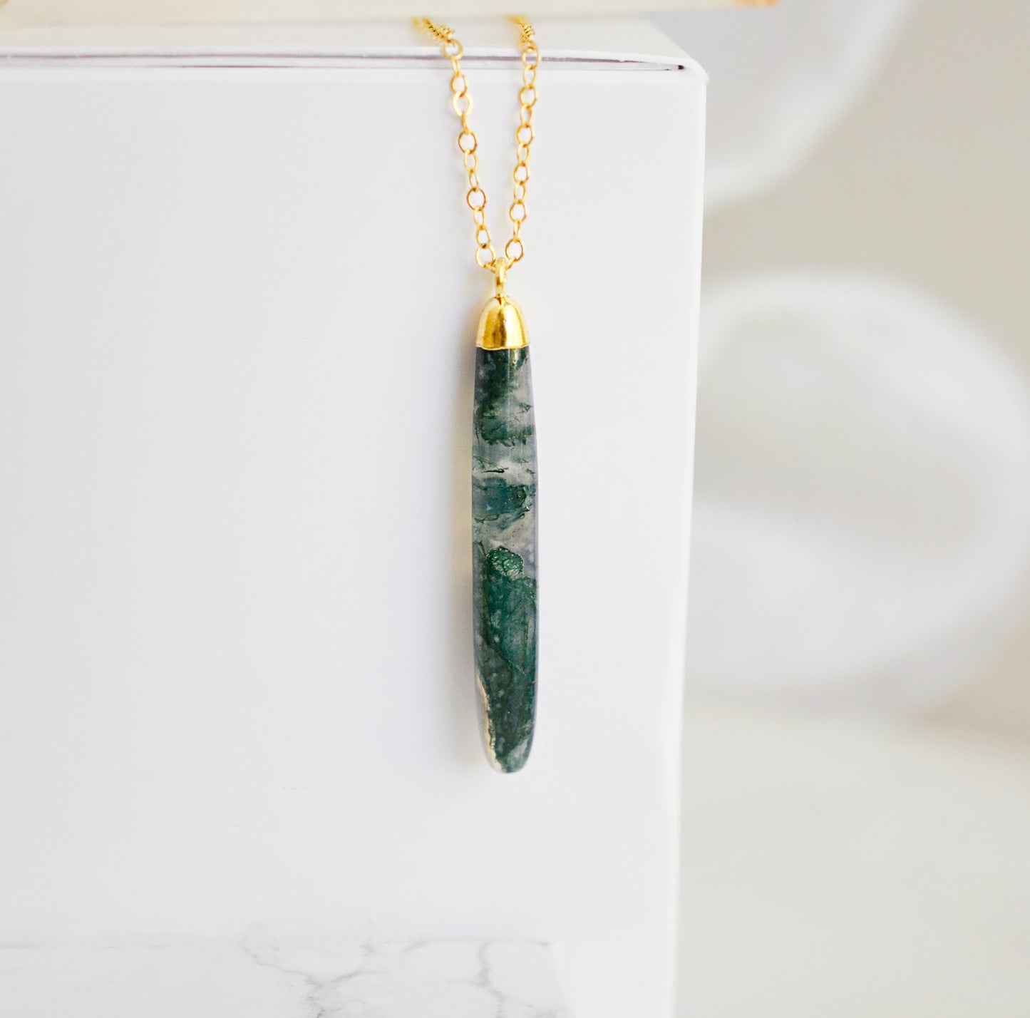 Long green, white, and clear real natural moss agate stone set on a 14k gold filled chain. The pendant is a long thin oval shape.