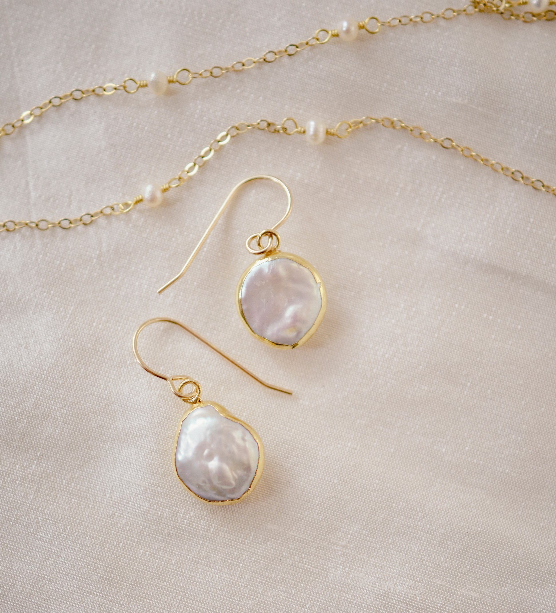 Natural white freshwater pearl dangle earring. The pearl is set in 22k gold electroplate and suspended from 14k gold filled earwires. Shown with our dainty pearl necklace.