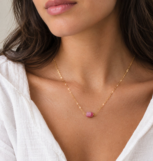 A woman wearing a natural, raw pink tourmaline crystal suspended on a sparkling 14k gold filled chain. The stones are rough and organic. This dainty handmade necklace is also available in sterling silver. 