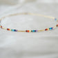 Tiny stones arranged in the order of the seven chakras or rainbow colors. Colors include: purple, blue, aqua, green, yellow, orange, and red. Close up of the gold style.