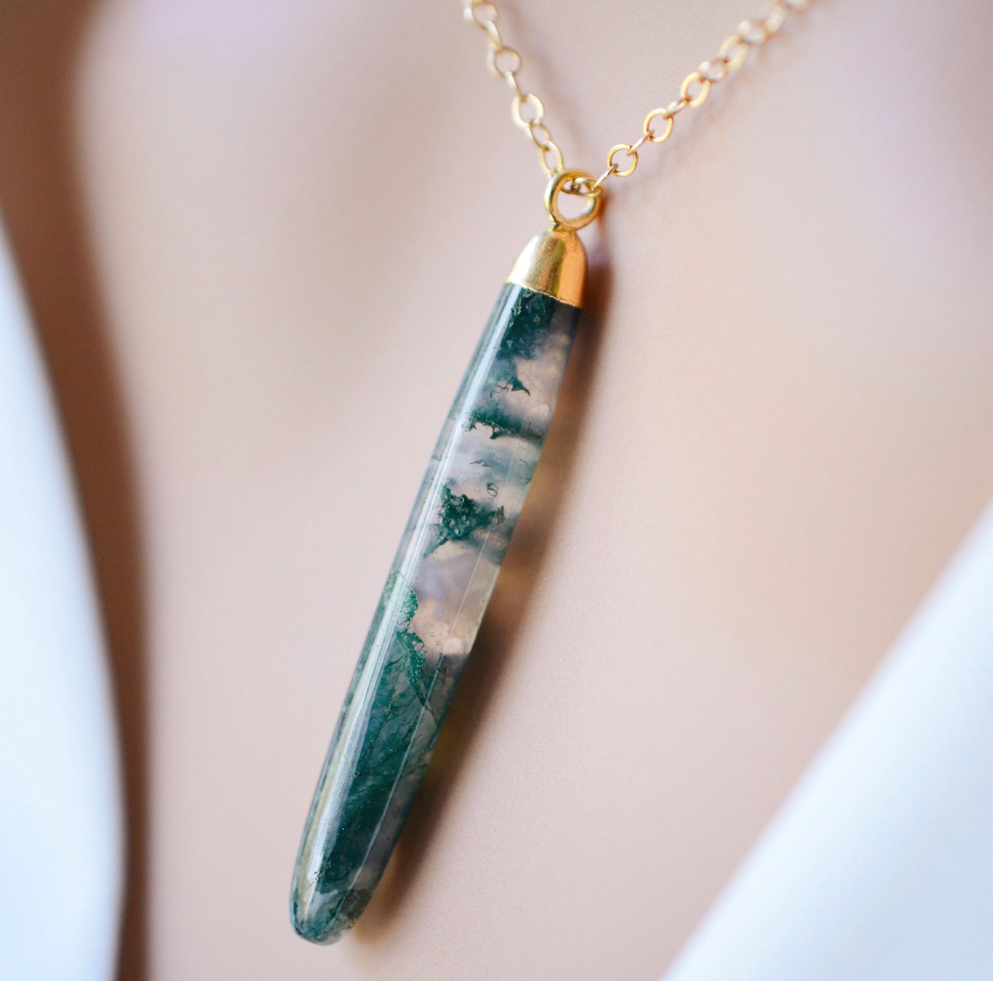 Long green, white, and clear real natural moss agate stone set on a 14k gold filled chain. The pendant is a long thin oval shape. Close Up.