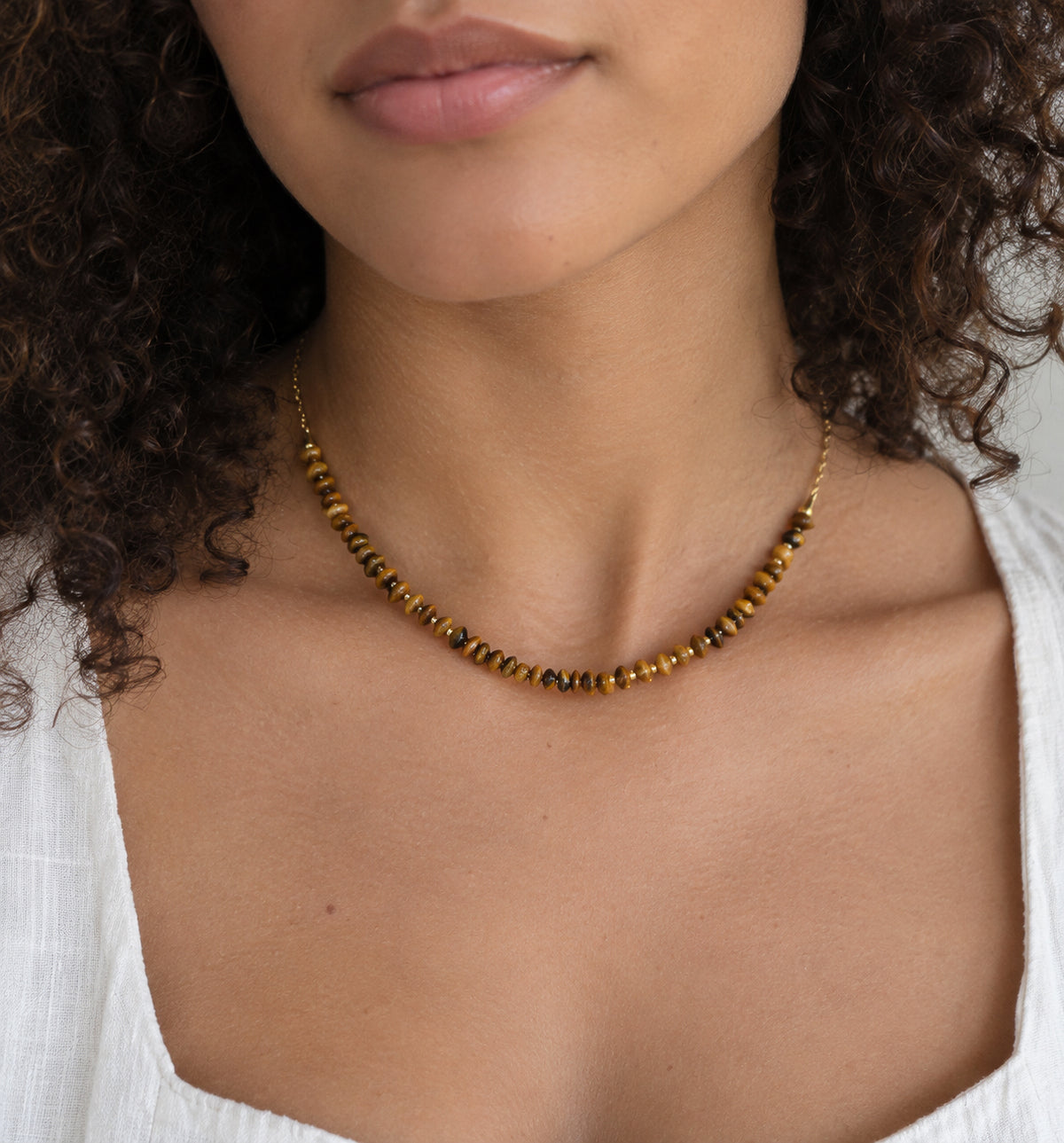 A woman wearing a beaded tiger eye stone necklace in gold. The gemstones are natural and genuine smooth polished. Jewelry is handmade in Connecticut by Gemnia.