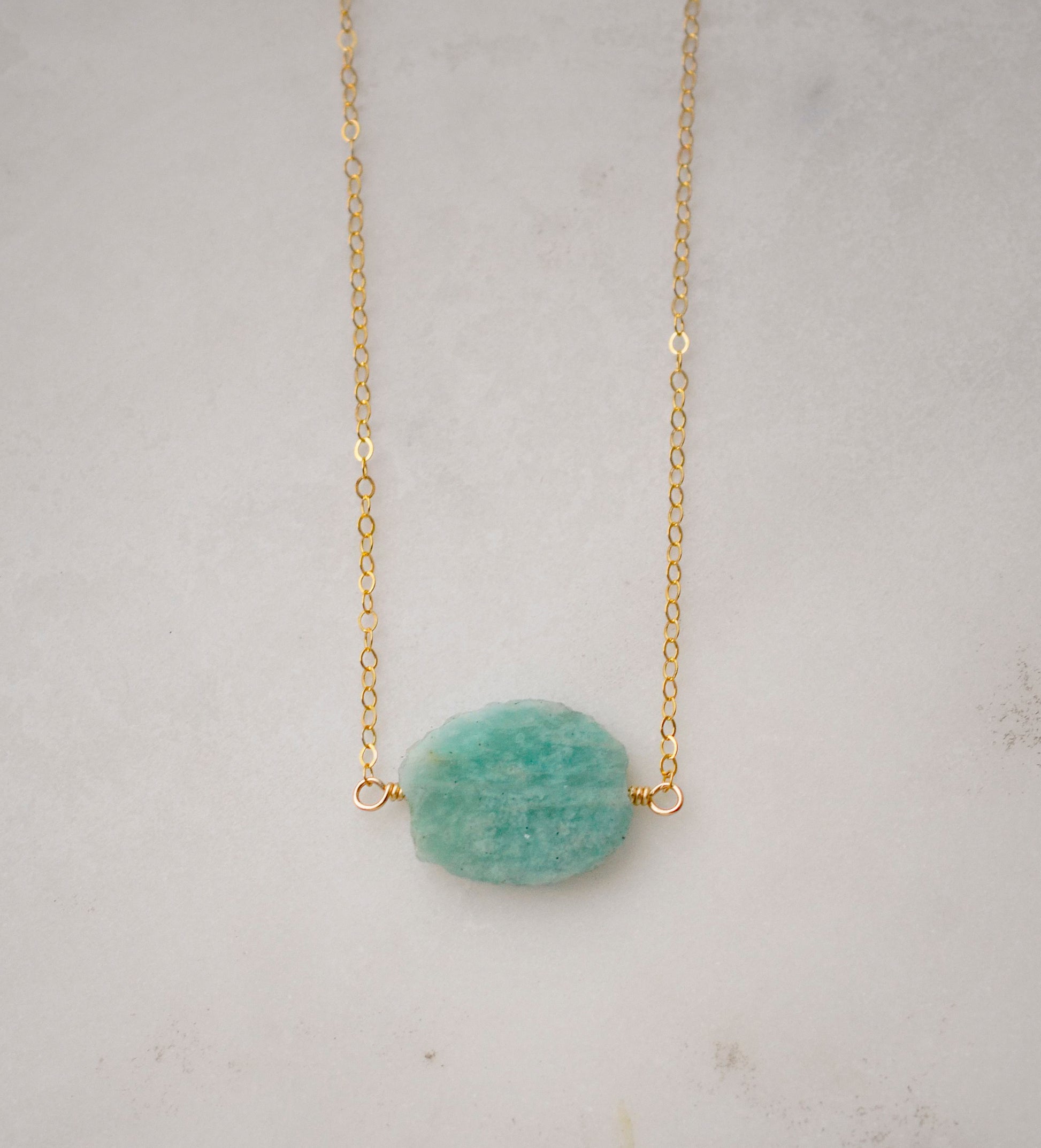 Aqua blue amazonite slice gemstone set onto a 14k gold filled chain. The stone is semi oval in shape, but irregular. It's smooth polished, but with raw edges.