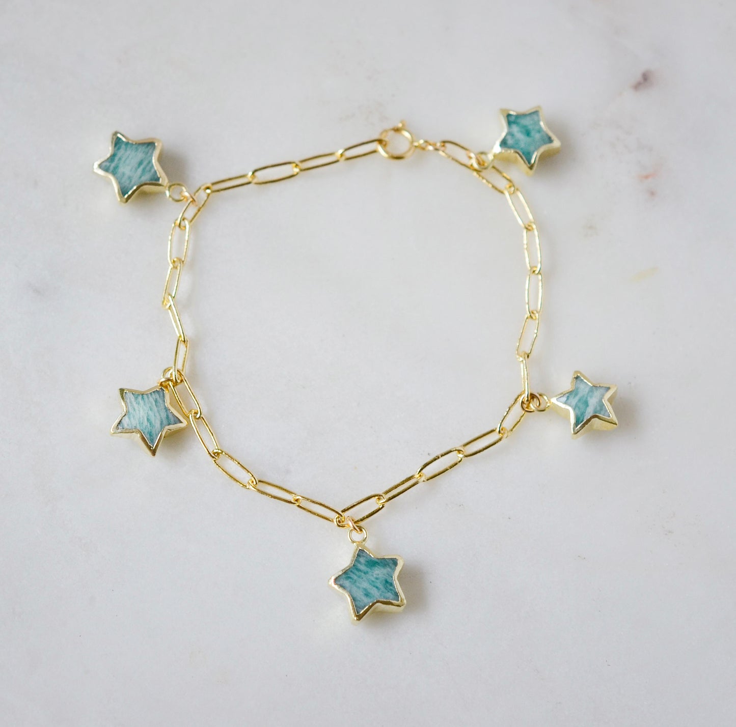 Gold bracelet with blue amazonite star-shaped gemstone charms on a light gray background.