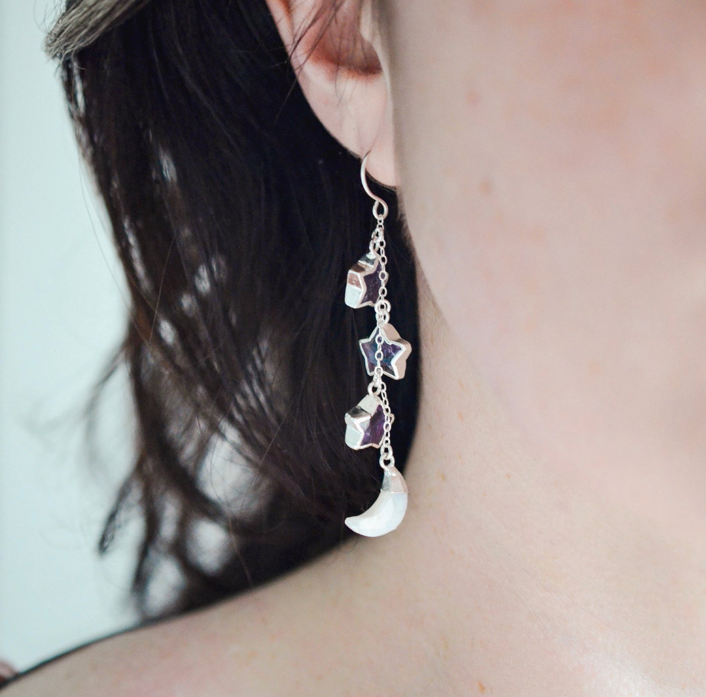 Three natural purple amethyst gemstone stars dangle atop rainbow moonstone crescent moons in these earrings. Shown in sterling silver. Modeled image.