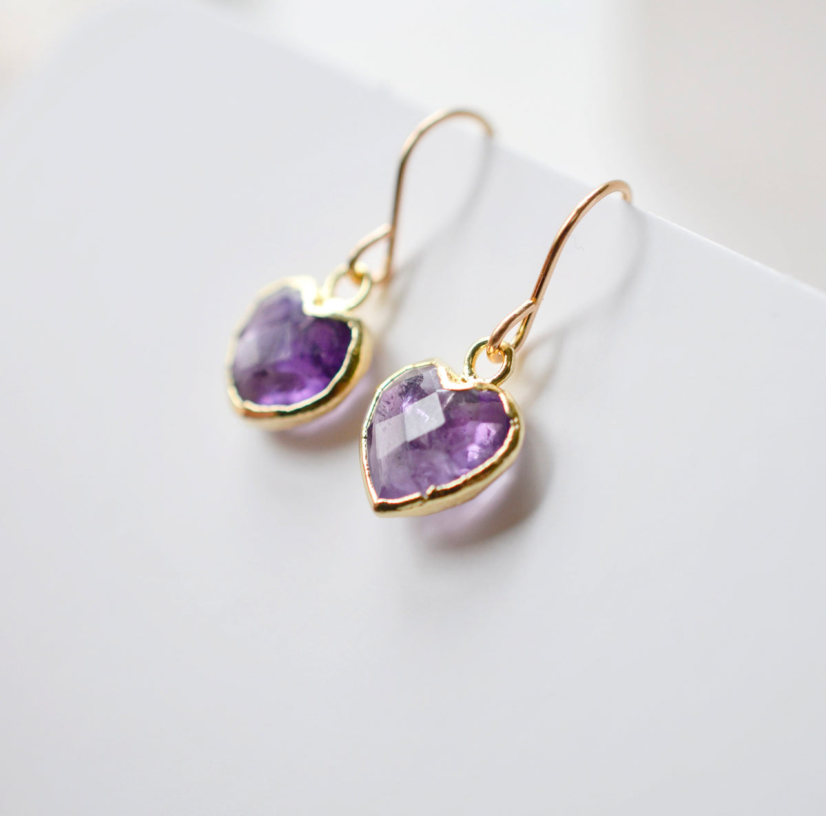 A closeup of natural purple amethyst heart dangle earrings in gold. The french earwires are 14k gold filled. Handmade in Connecticut. 