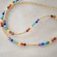 Tiny stones arranged in the order of the seven chakras or rainbow colors. Colors include: purple, blue, aqua, green, yellow, orange, and red. Close up of the gold style.