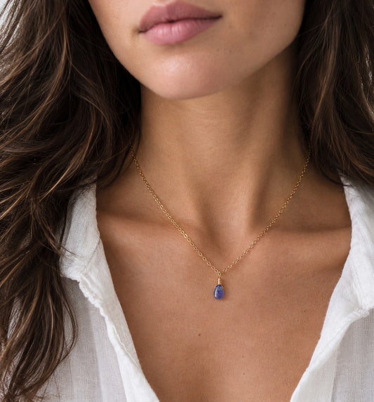 A woman wearing a minimalist genuine tanzanite gemstone droplet on a 14k gold filled chain. The natural gem is smooth polished and periwinkle in color. Handmade in Connecticut by Gemnia.