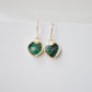 Raw emerald heart earrings in gold. The stones are bezeled in 22k gold then set on gold earwires. The gemstone colors range in dark greens with hints of white or black.