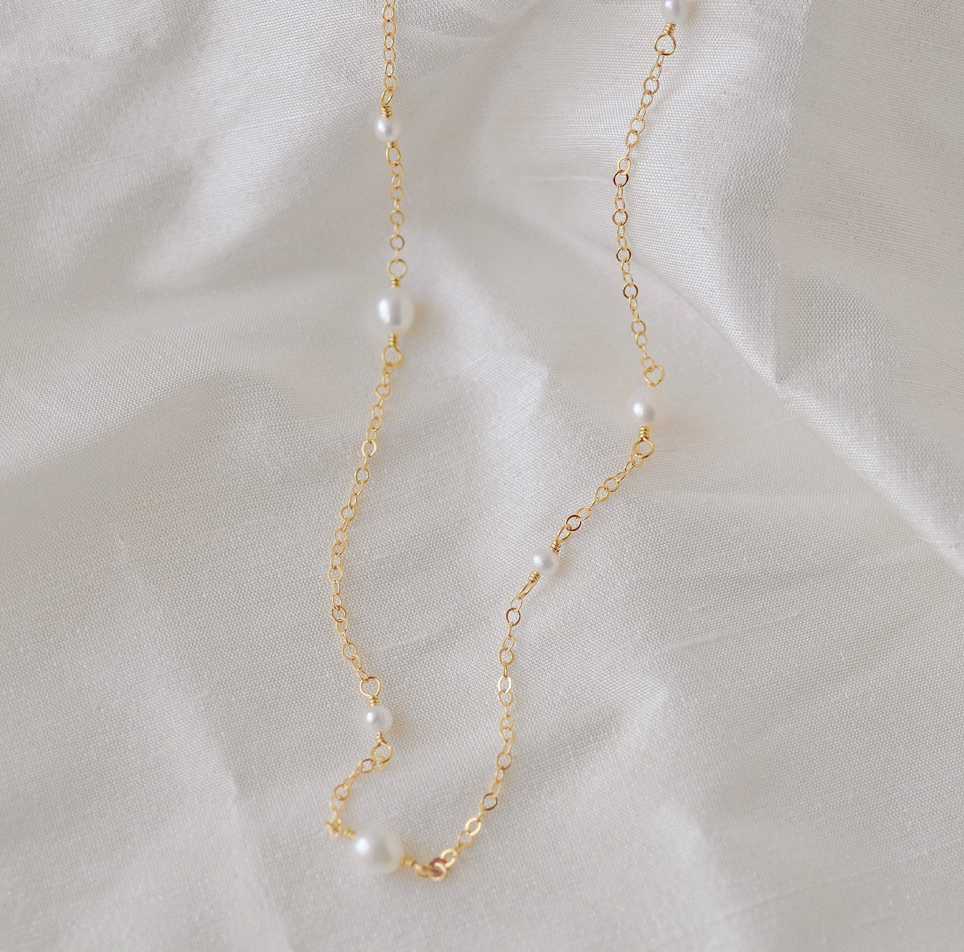 Genuine white freshwater pearls of varying sizes alter on this chain necklace. The gold style is shown.