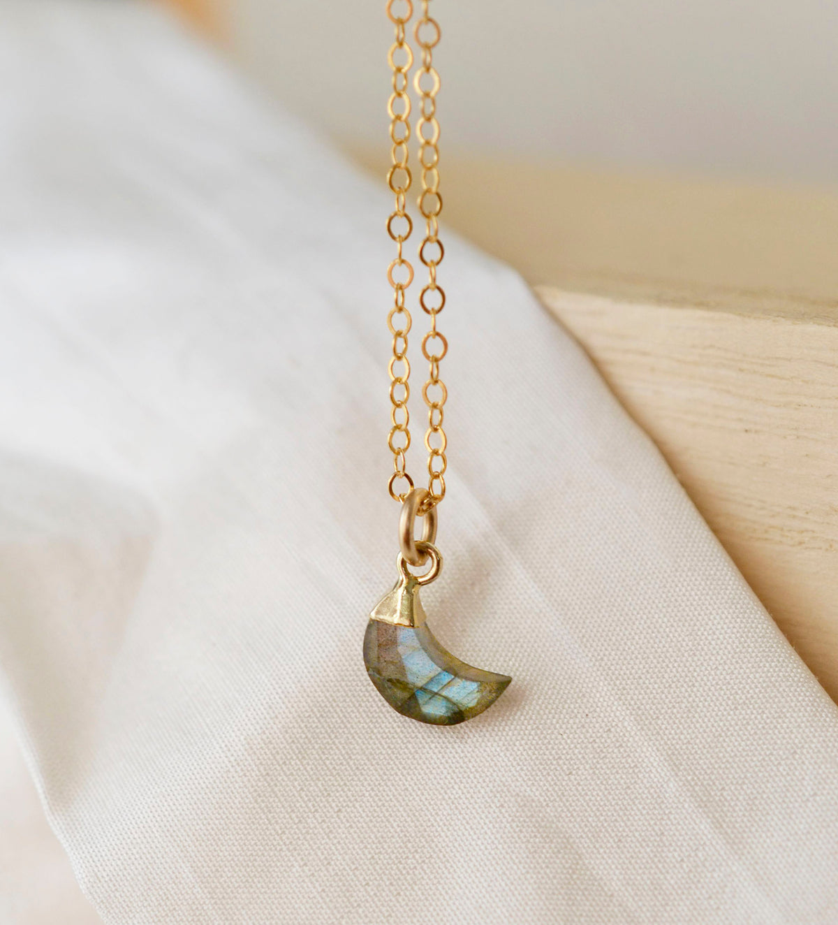 A minimalist, dainty crescent moon pendant handmade from natural labradorite gemstone, set on a 14k gold filled chain. Made in Connecticut by Gemnia.