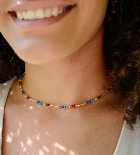 Tiny stones arranged in the order of the seven chakras or rainbow colors. Colors include: purple, blue, aqua, green, yellow, orange, and red. Modeled image. Handmade in Connecticut by Gemnia Jewelry.