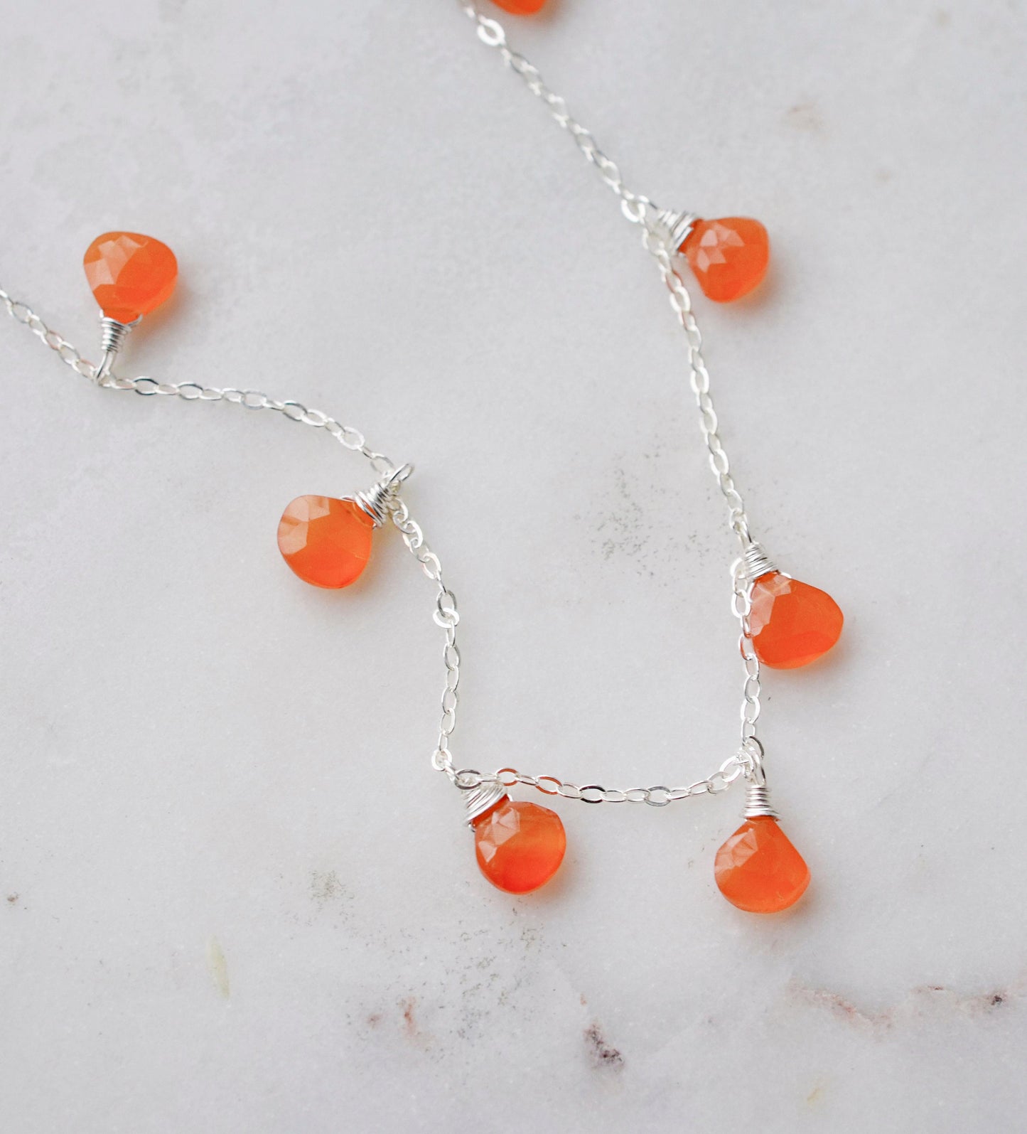 Close up of the genuine orange carnelian crystals set on a sterling silver chain necklace.