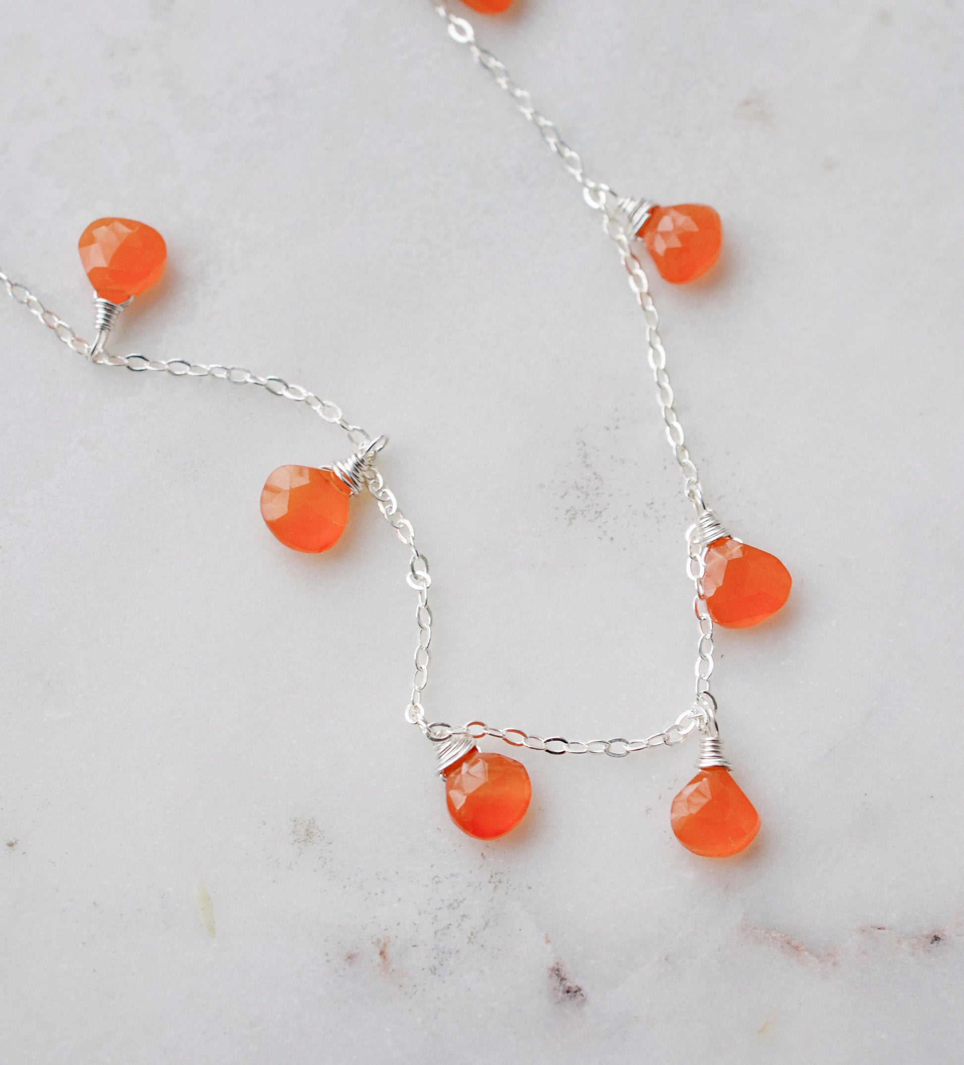 Close up of the genuine orange carnelian crystals set on a sterling silver chain necklace.