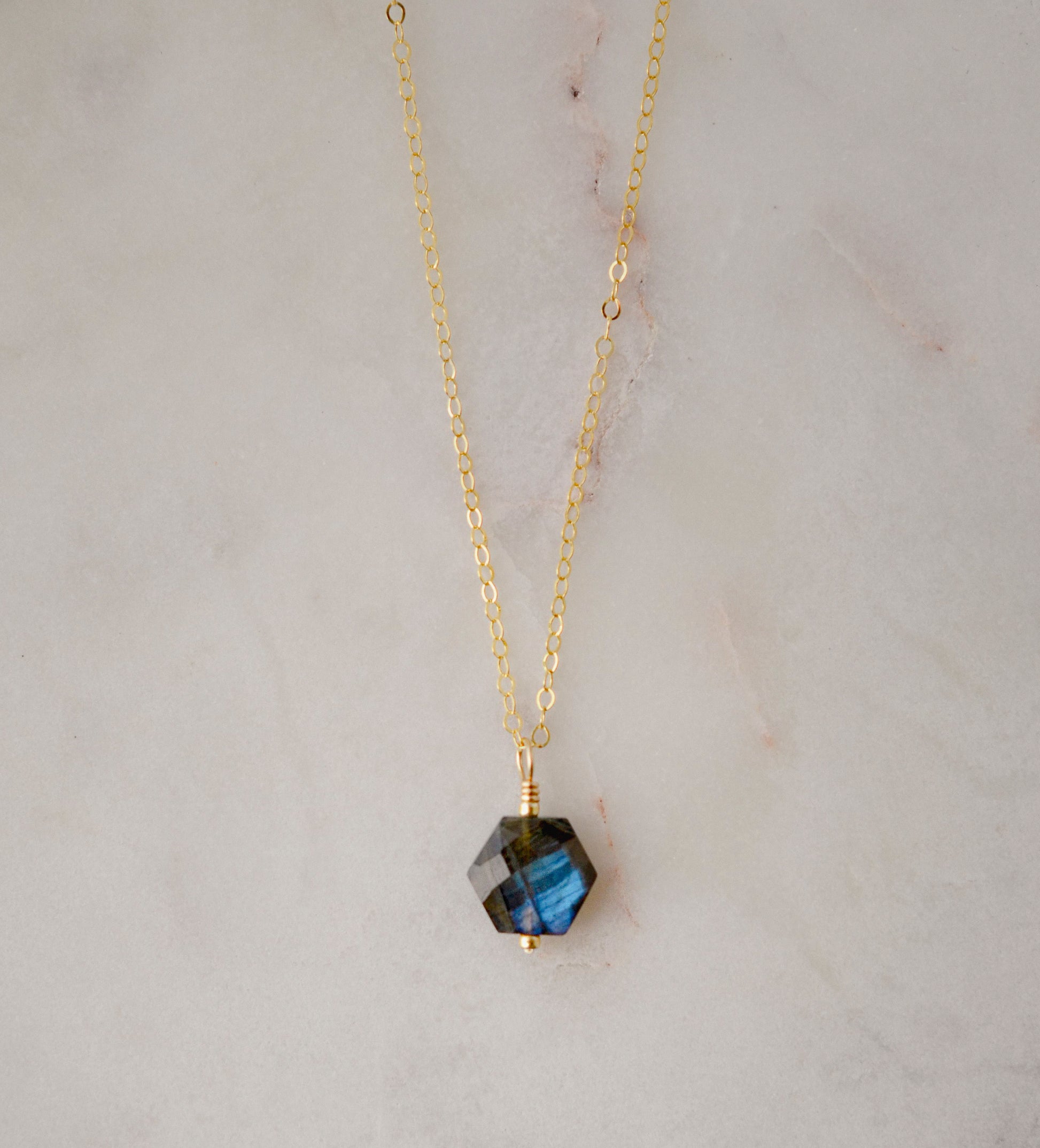 Blue flashing labradorite pendant cut into a hexagonal shape and suspended onto a gold chain.
