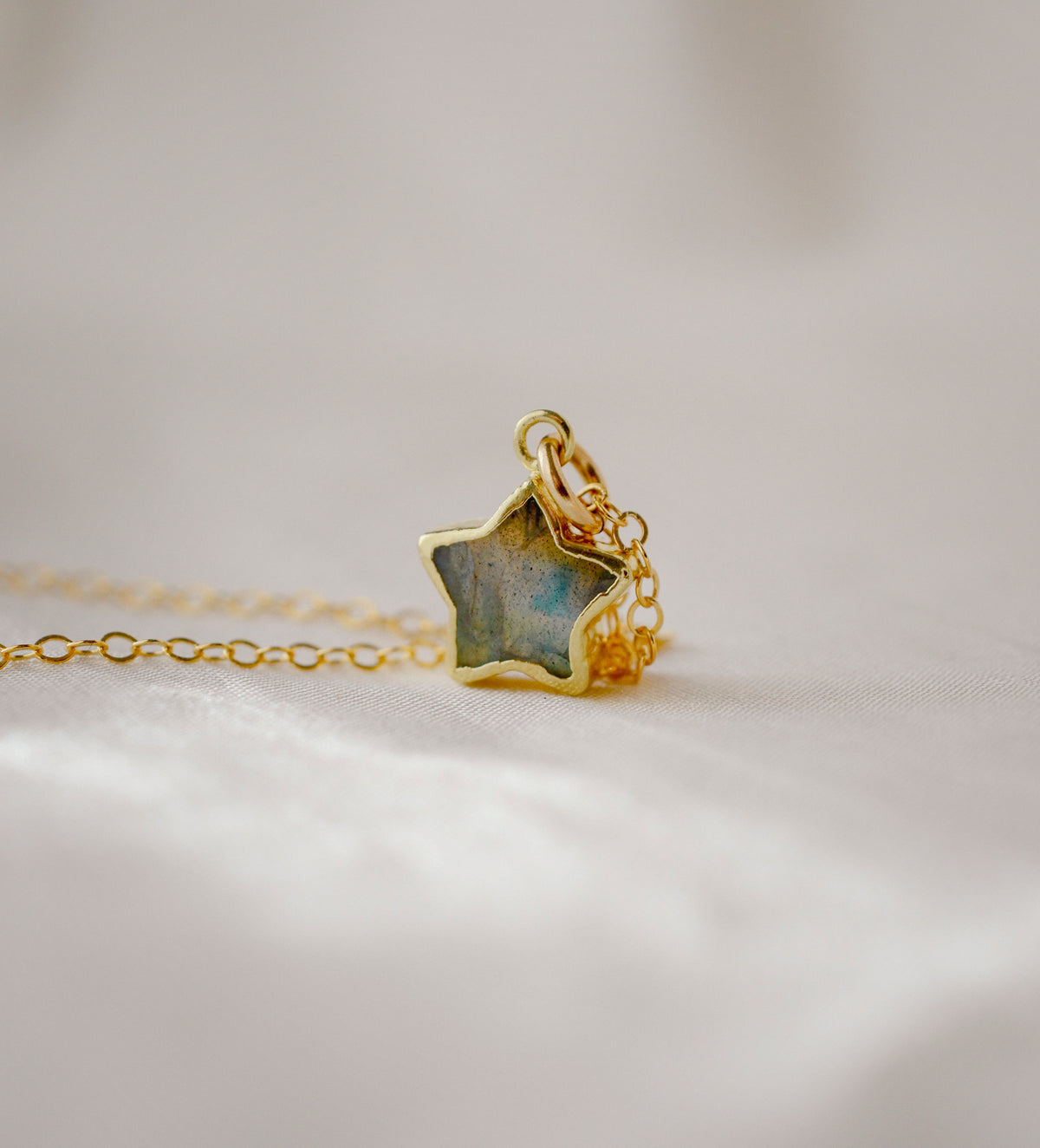 A close up image of a dainty handmade labradorite gemstone star pendant set on a 14k gold filled chain.