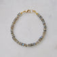 Blue flashing natural heishi or wheel shaped Labradorite gemstones strung together onto a bracelet. Tiny gold beads act as spacers between the stones. The gold style is shown.