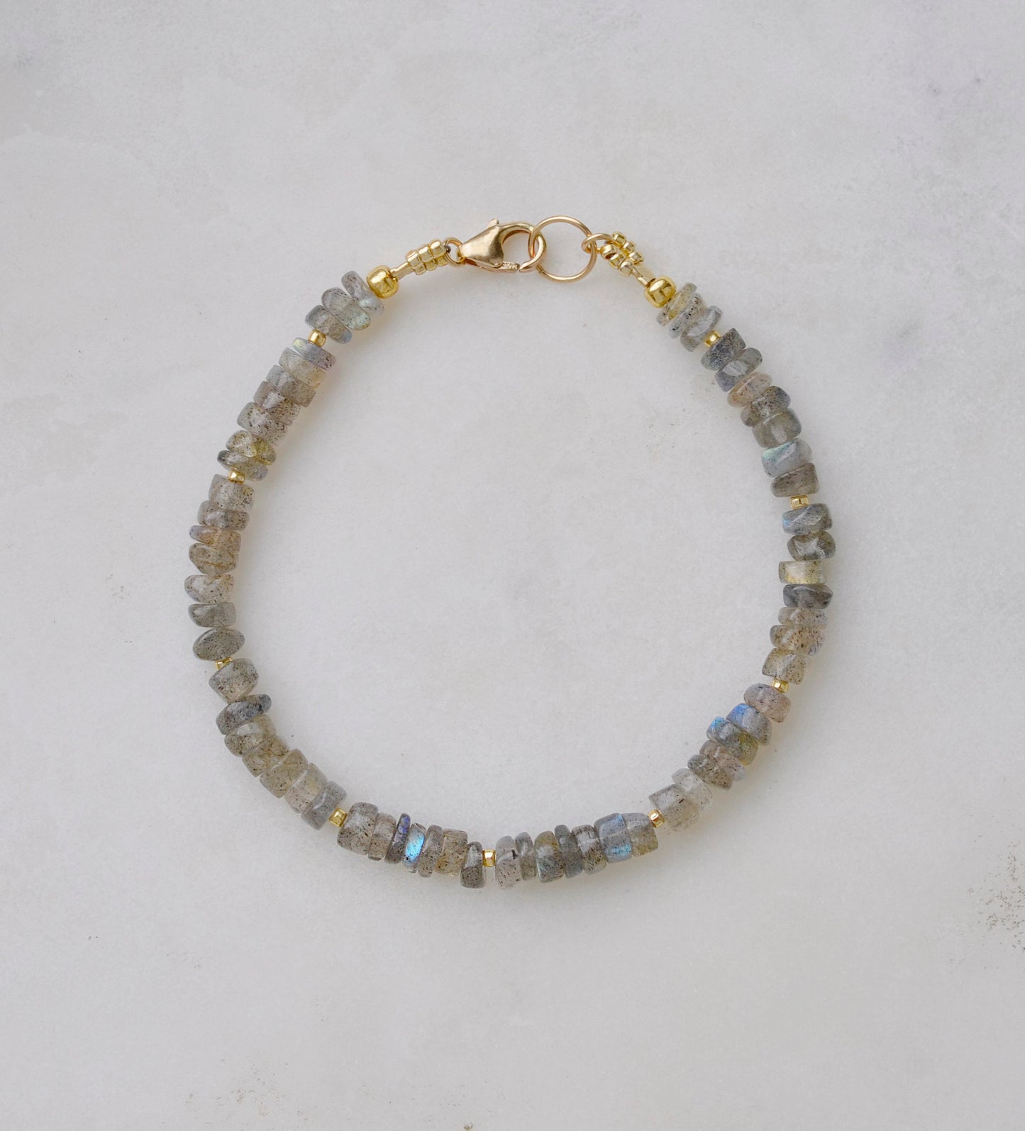 Blue flashing natural heishi or wheel shaped Labradorite gemstones strung together onto a bracelet. Tiny gold beads act as spacers between the stones. The gold style is shown.