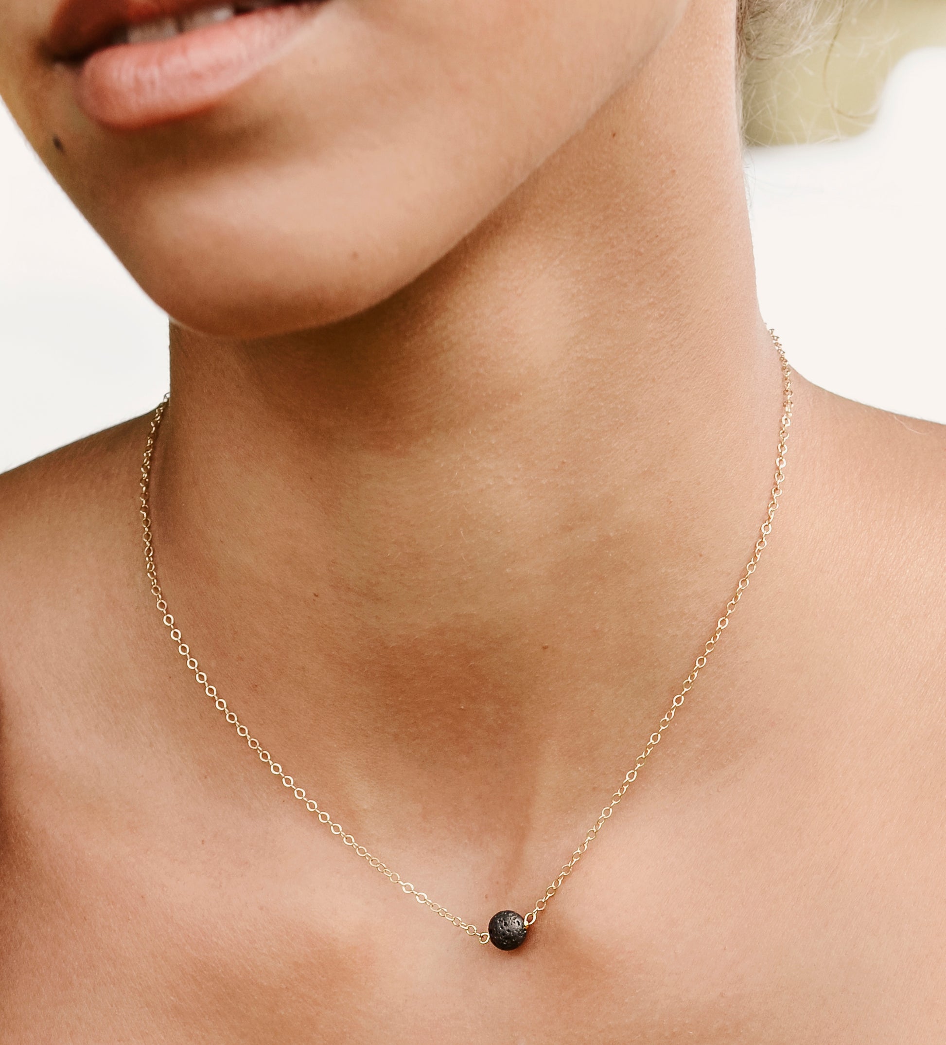Handmade genuine black lava round stone placed onto a 14k gold filled chain. Modeled image.