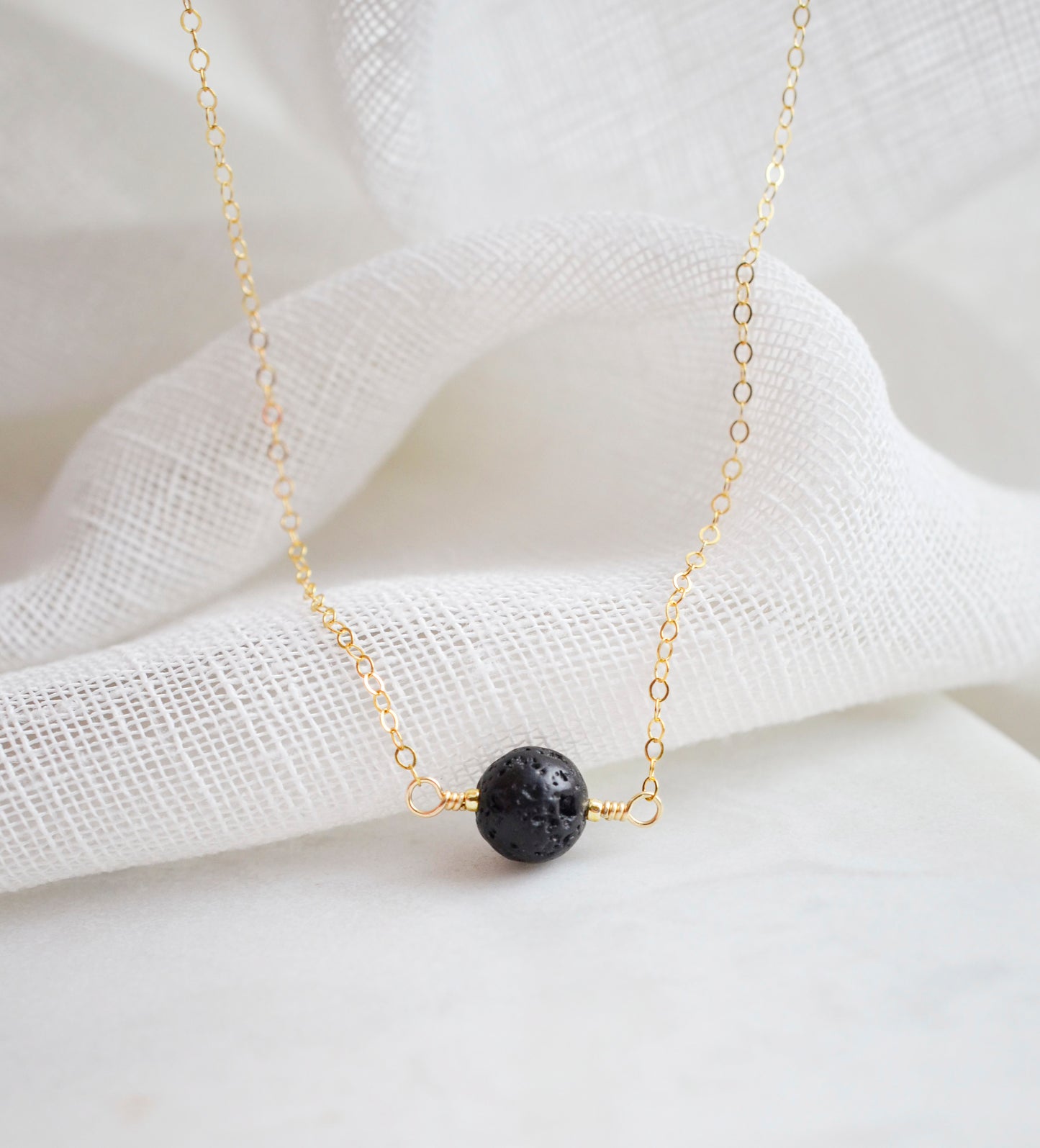 Close up image of a black Lava stone set onto a 14k gold filled chain. The stone is round with an irregular surface. 