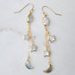 Long gold dangle earrings with star and moon charms on a light background. The stones are freshwater pearl, labradorite, and mother of pearl.
